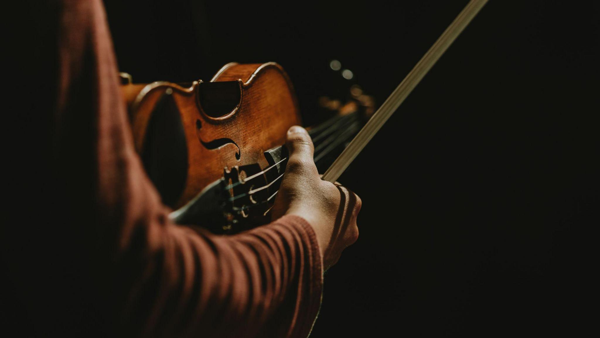 A dark moody stock image of a man's arm carrying a violin