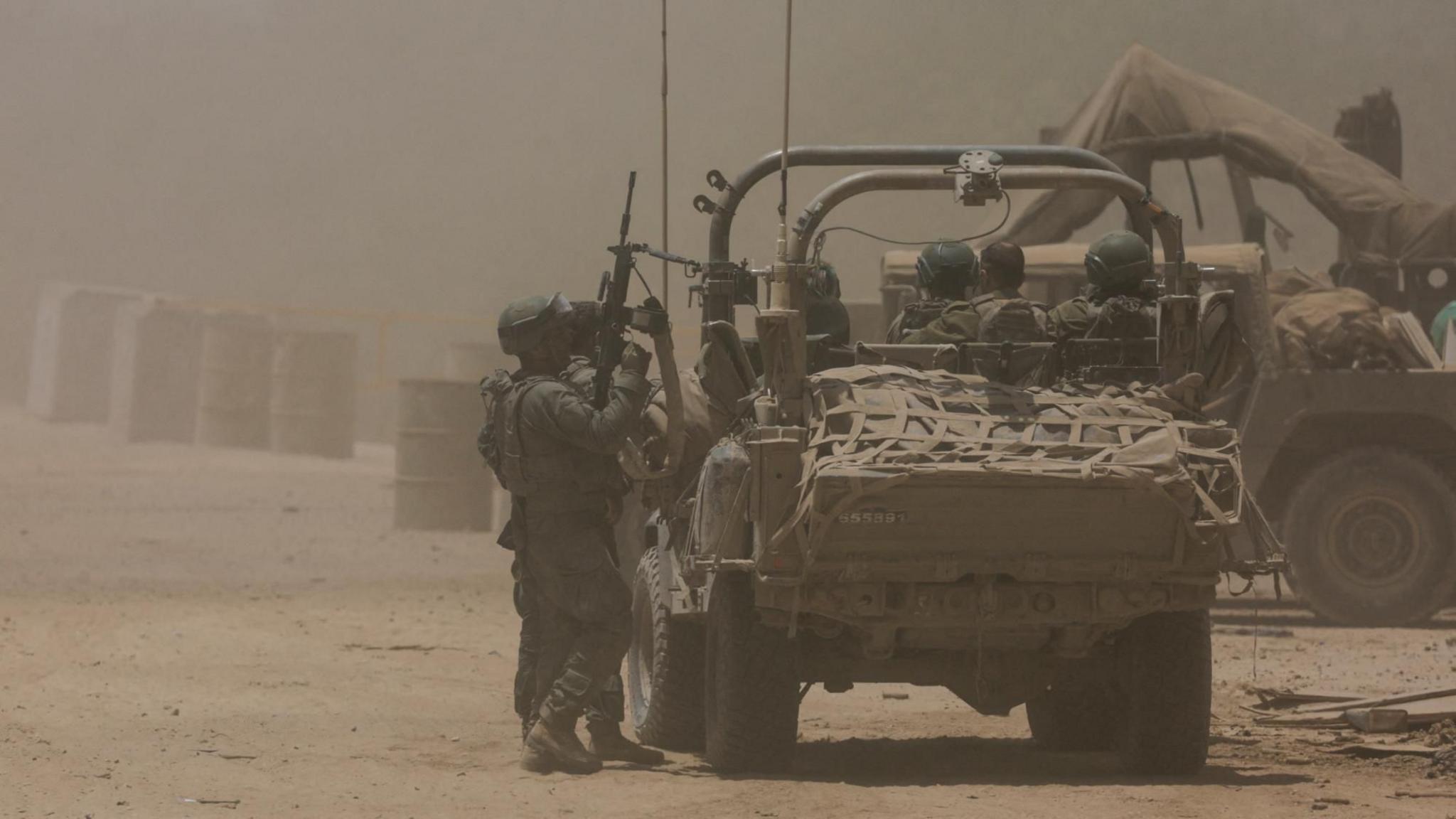 Israeli soldiers stand next to a military vehicle, near the Israel-Gaza border (2 July 2024)