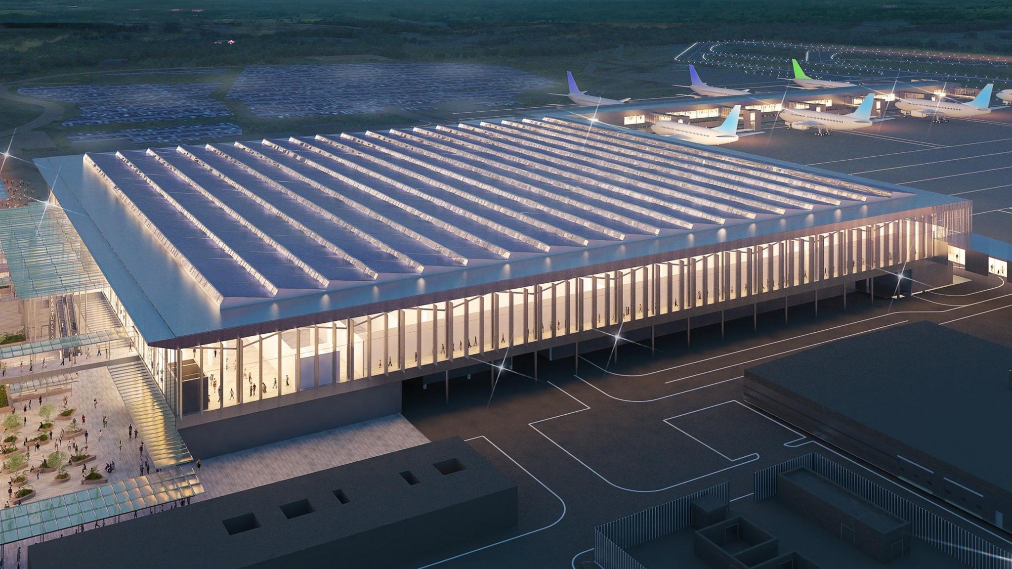 A computer-generated image of what the new terminal building could look like at London Luton Airport. Planes are parked on a nearby runway. The terminal is brightly lit rectangular building with glass sides.