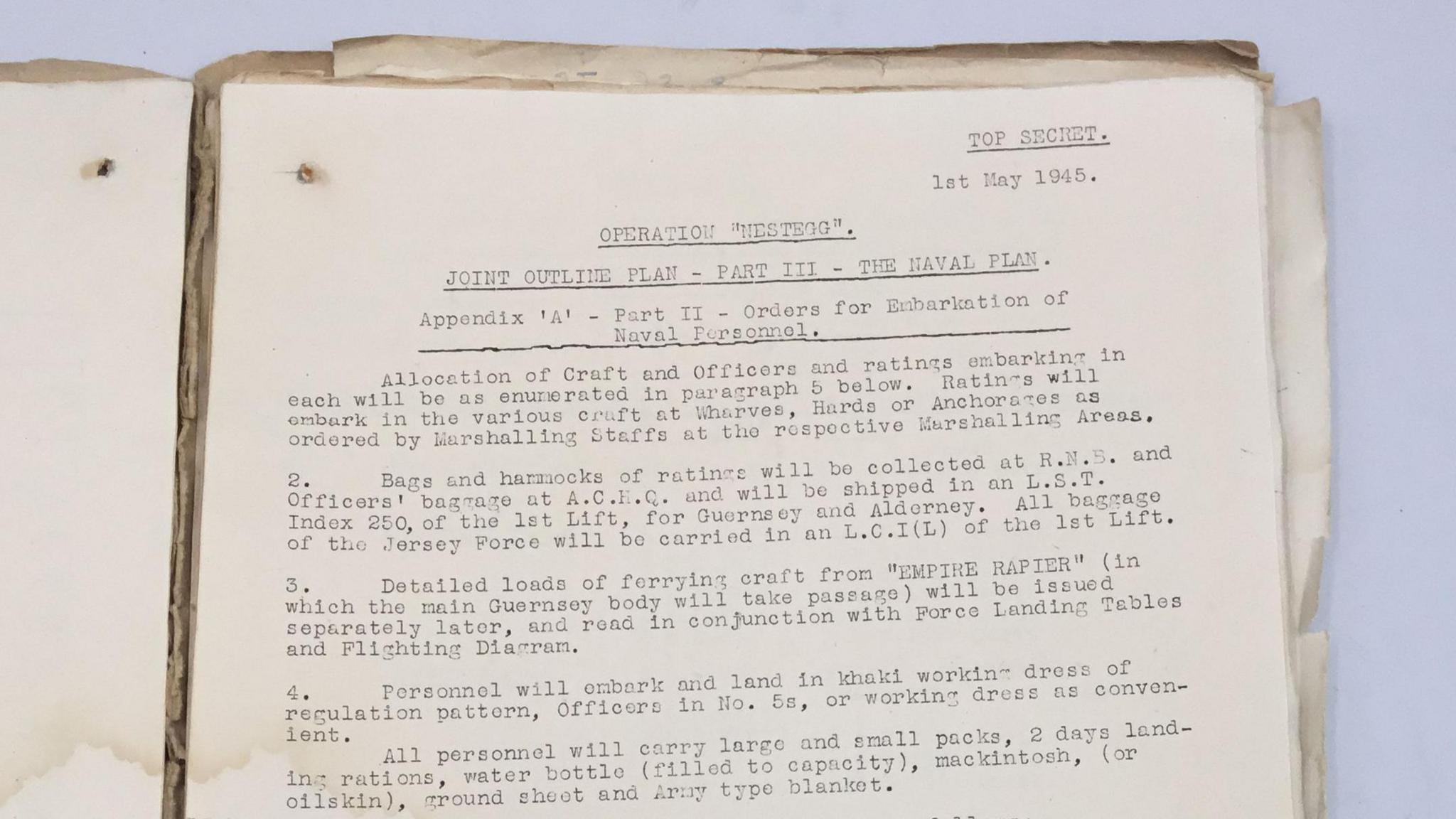An old document in a manila folder. It reads: 
TOP SECRET.
Ist May 1945.
OPERATION "NESTEGG". JOINT OUTLINE PLAN - PART ITI - THE NAVAL PLAN 
Appendix 'A' - Part II - Orders for Enbarkation of - Naval Personnel.
Allocation of Craft and Officers and ratings embarking in
each will be as enumerated in paragraph 5 below.
Ratings will embark in the various craft at Wharves, Hards or Anchorages as
ordered by Marshalling Staffs at the rospoctive Marshalling Areas.
Bags and harmocks of ratings will be collected at R.N.5. and
Officers' bagrage at A.C.F.C. and will be shipped in an L.S.T.
Index 250, of the lst Lift, for Guernsey and Alderney.
All bagrage of the Jersey Force will be carried in an L.C.I (L) of the lst Lift.
Detailed loads of forrying craft from "EMPIRE RAPIER" (in
which the main Guernsey body will take passage) will be issued separately later, and read in conjunction with Force Landing Tables and Flighting Diarram.
4. Personnel will embark and land in khaki working dress of regulation pattern, Officers in No. 5s, or working dress as convenient.
All personnel will carry largo and small packs, 2 days landing rations, water bottle (filled to capacity), mackintosh, (or oilskin), ground sheet and Army type blanket.