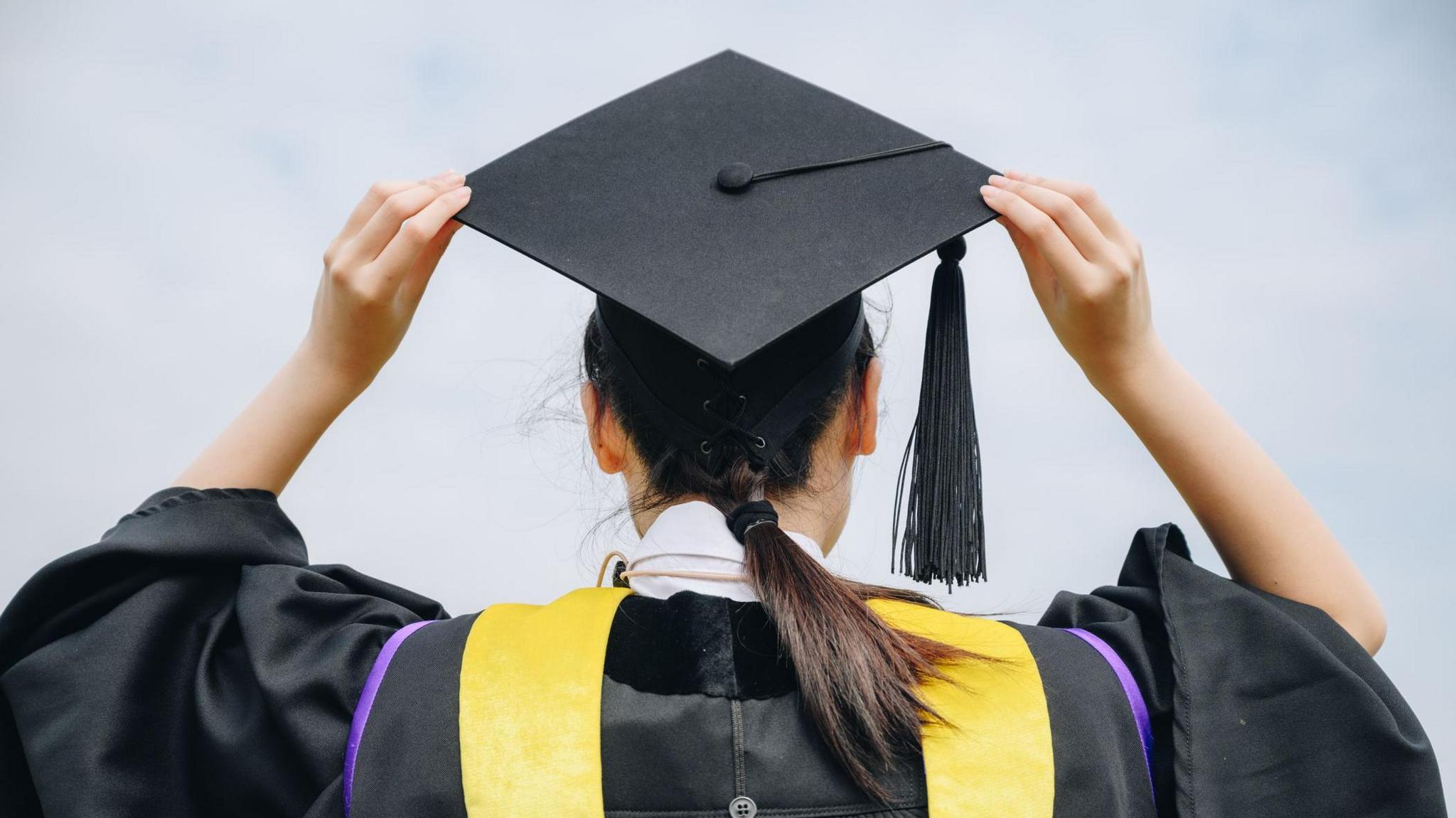 The picture shows the back of a girl's head and shoulders - she wears traditional university graduation attire cap and gown.