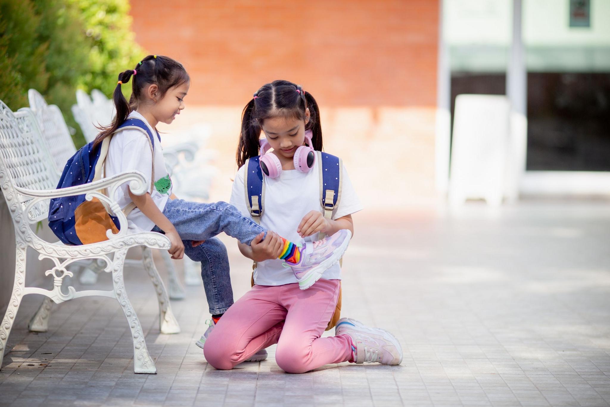A girl helping a friend to tie her laces.