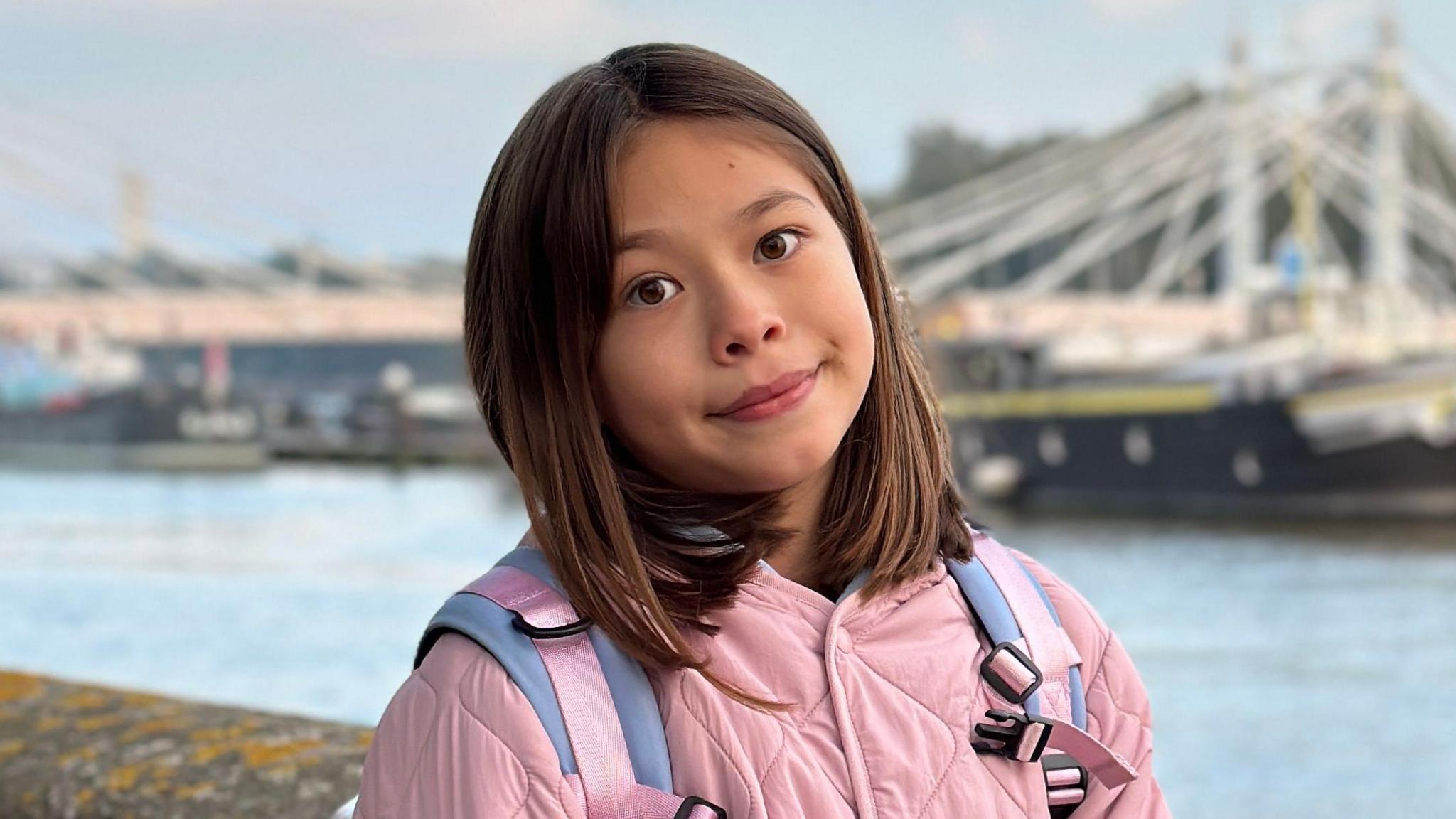 A nine-year-old girl stands on the banks of the River Thames overlooking a white bridge and boats.