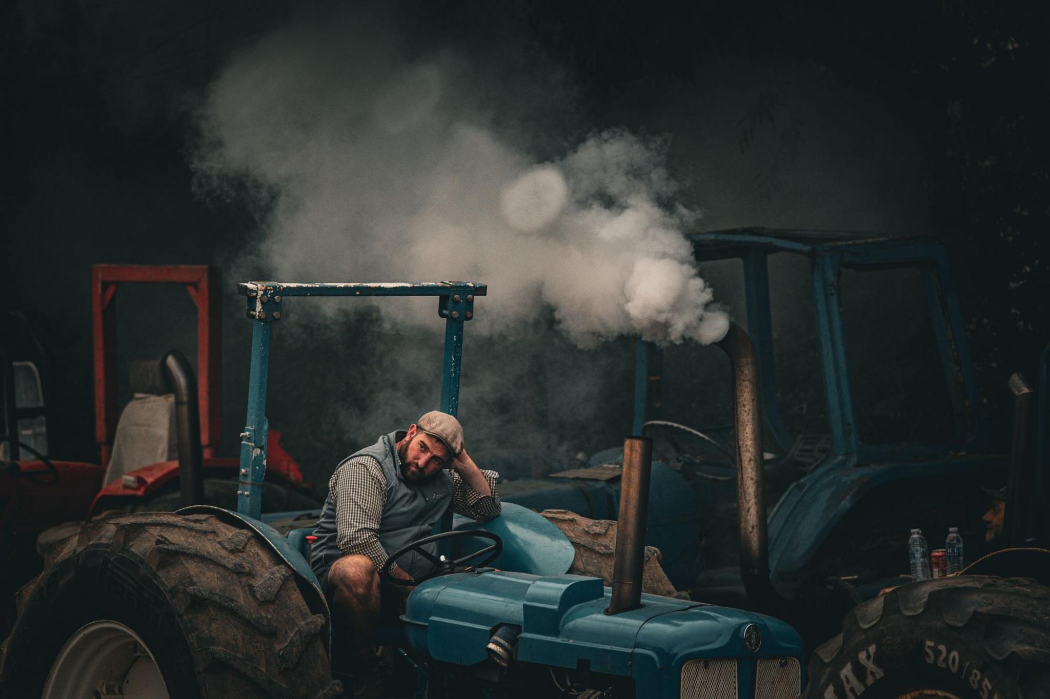 A farmer sits on his tractor with smoke coming from the exhaust