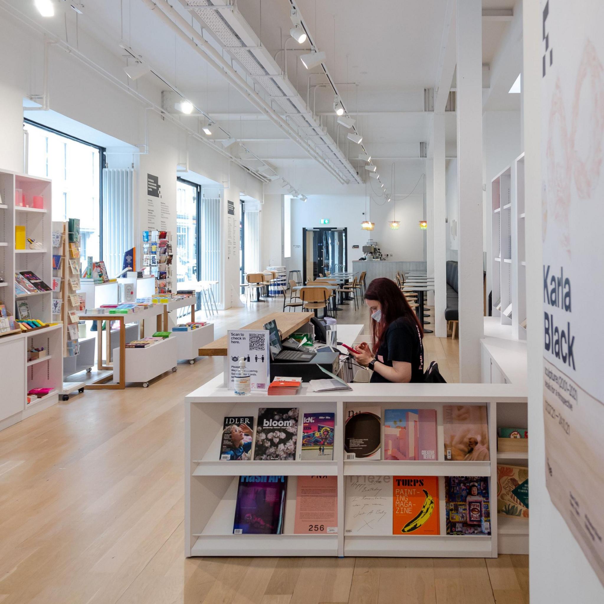 Gallery shop has light floors and white walls and a worker sits at a desk and a cash register