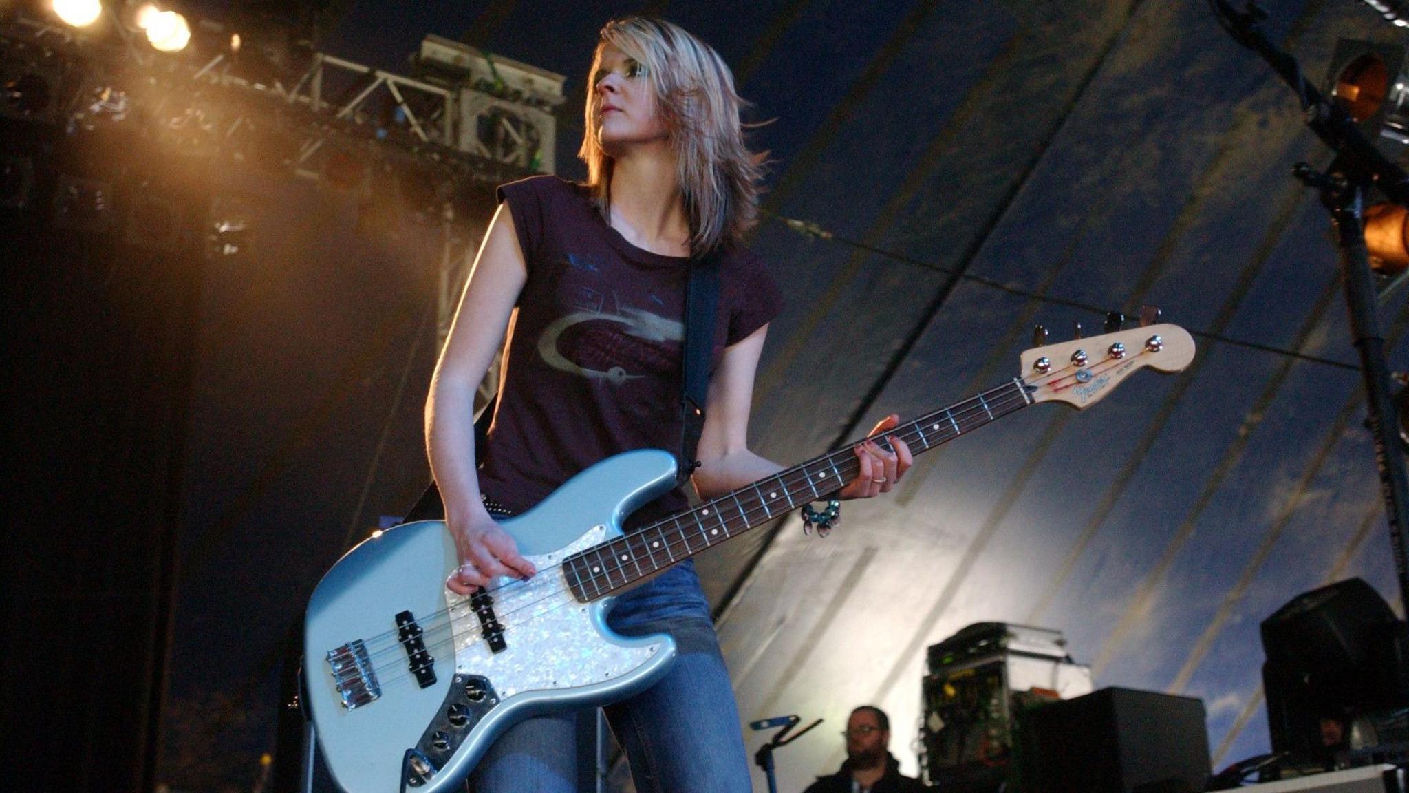 Charlotte Cooper from The Subways plays a bass guitar. She has shoulder length blonde and brown hair.