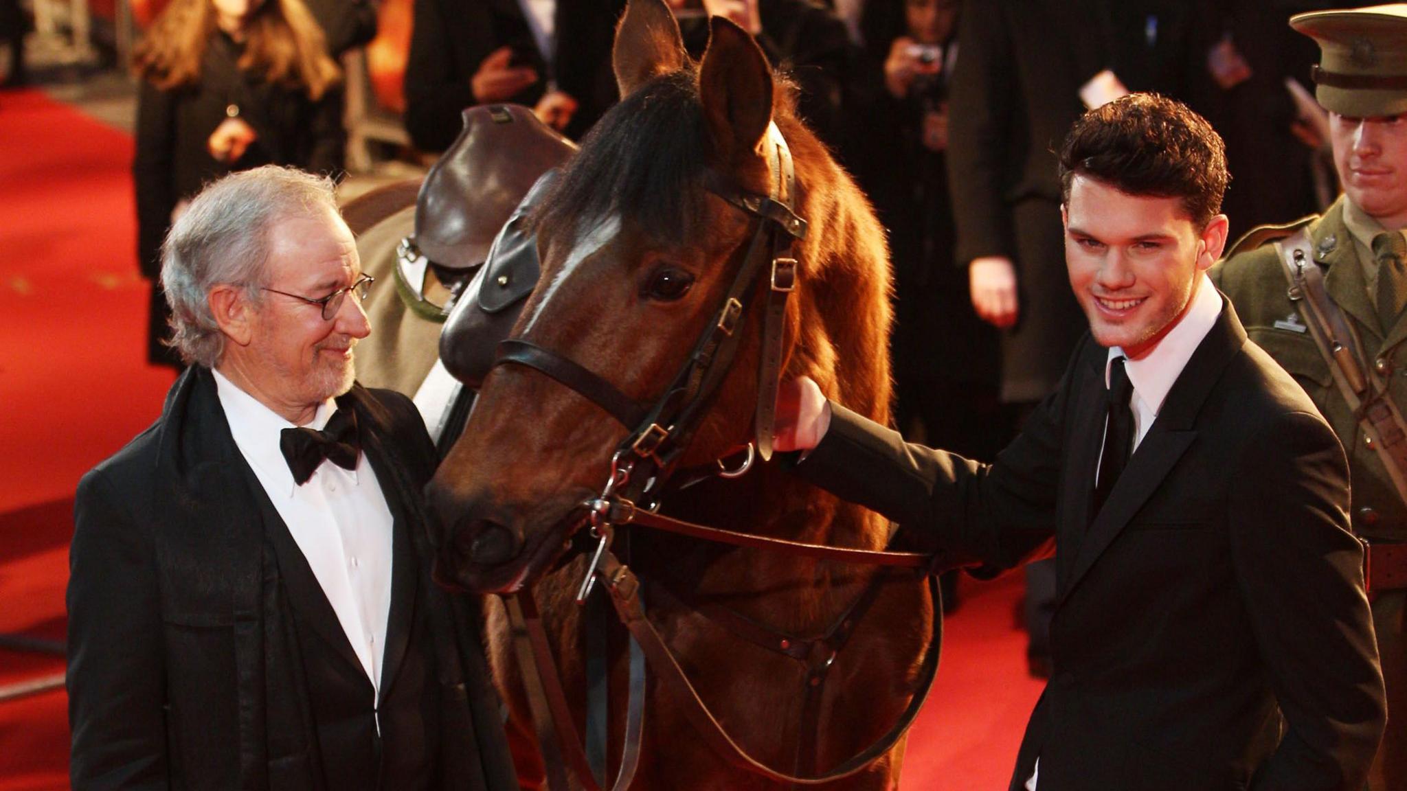 Steven Spielberg and actor Jeremy Irvine with 'Joey' the horse at the UK Royal film premiere of War Horse at the Odeon West End in London. Steven and Jeremy are wearing black suits.
