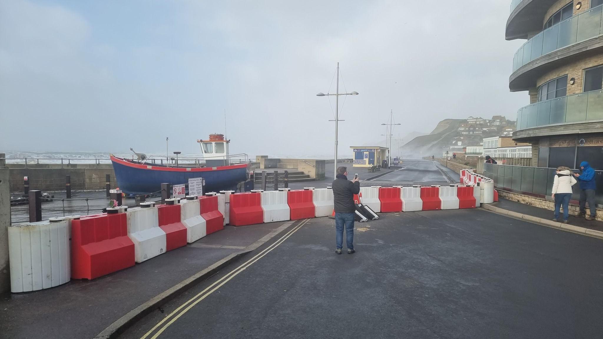 A man filming the red and white barriers that have been put up on the seafront