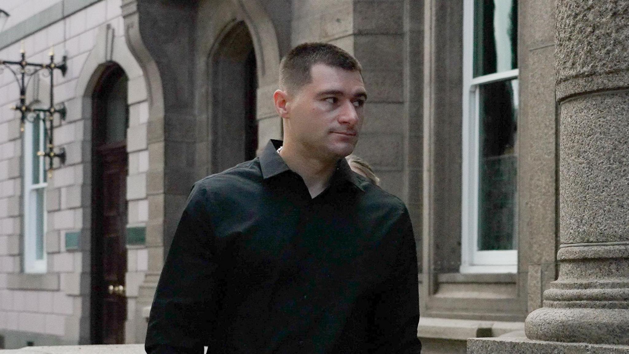 A man wearing a black shirt heading into the royal court building.