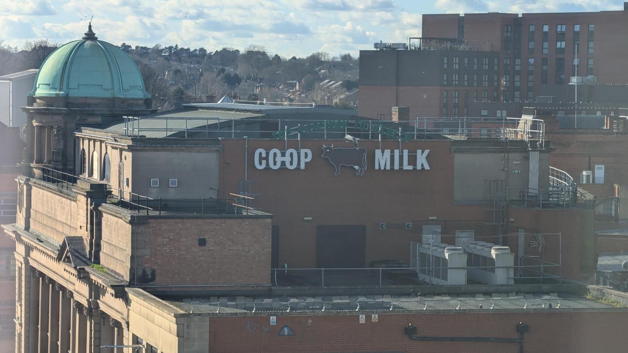 A photo of a sign saying "Co-op Milk" during the day, with a cow figure in the middle