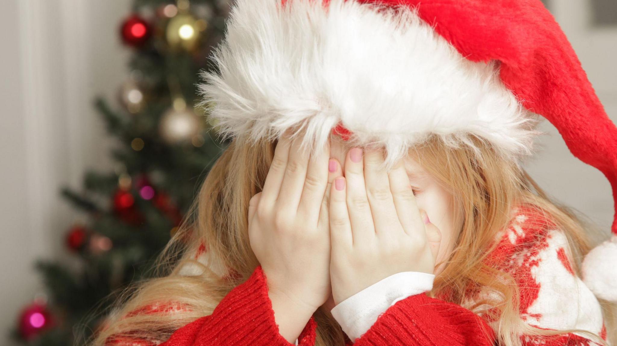 Sad, frustrated little girl in Christmas outfit and Santa hat