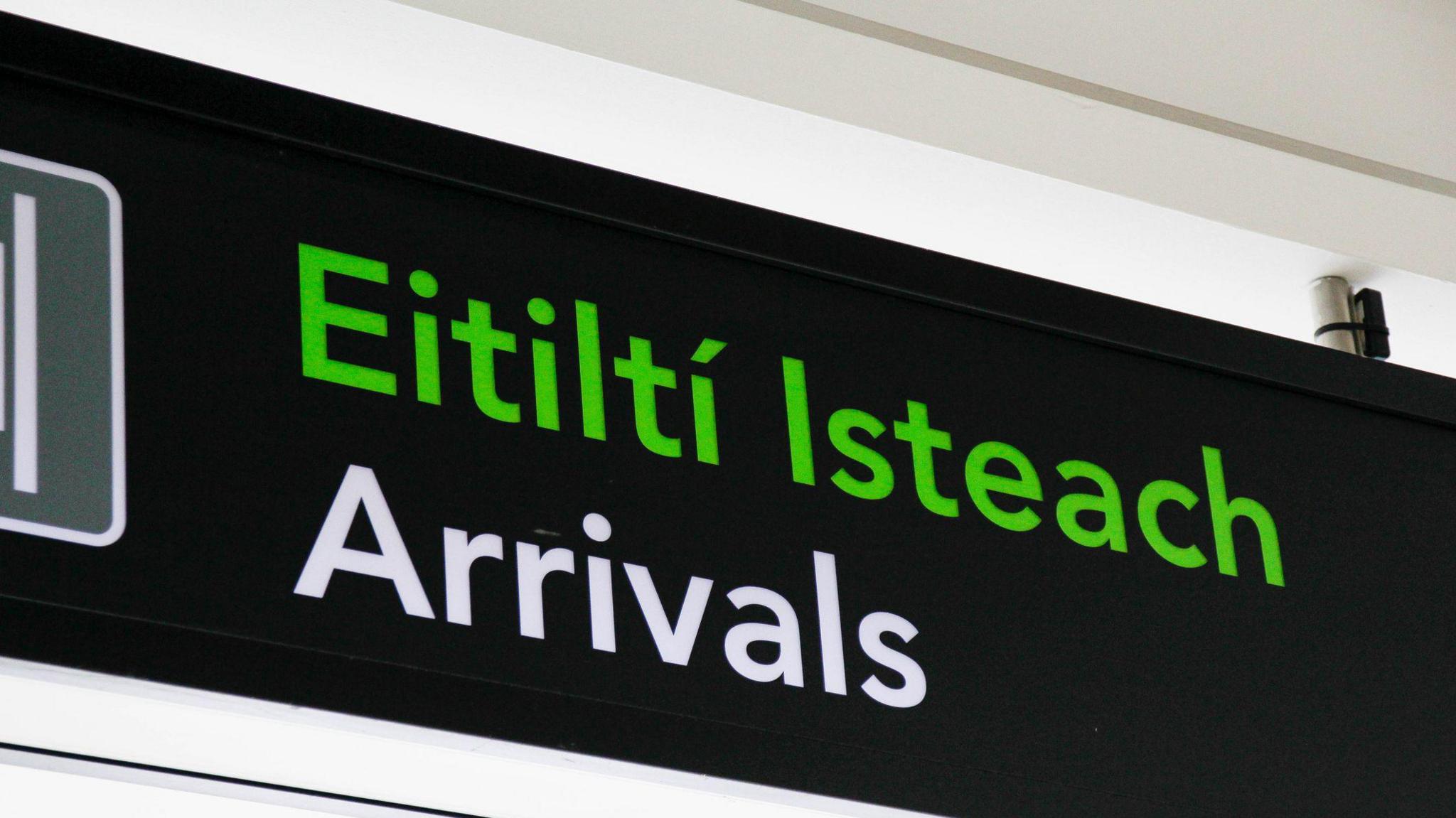 Arrivals sign at Dublin airport. Arrivals is written in green in Irish, and below in English in white, on a black sign. 