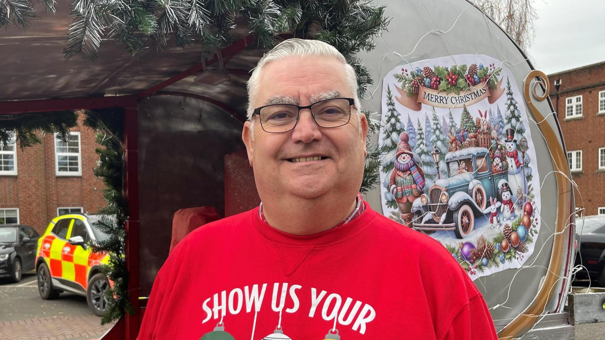 Man wearing a red Christmas jumper stood in front of a sleigh