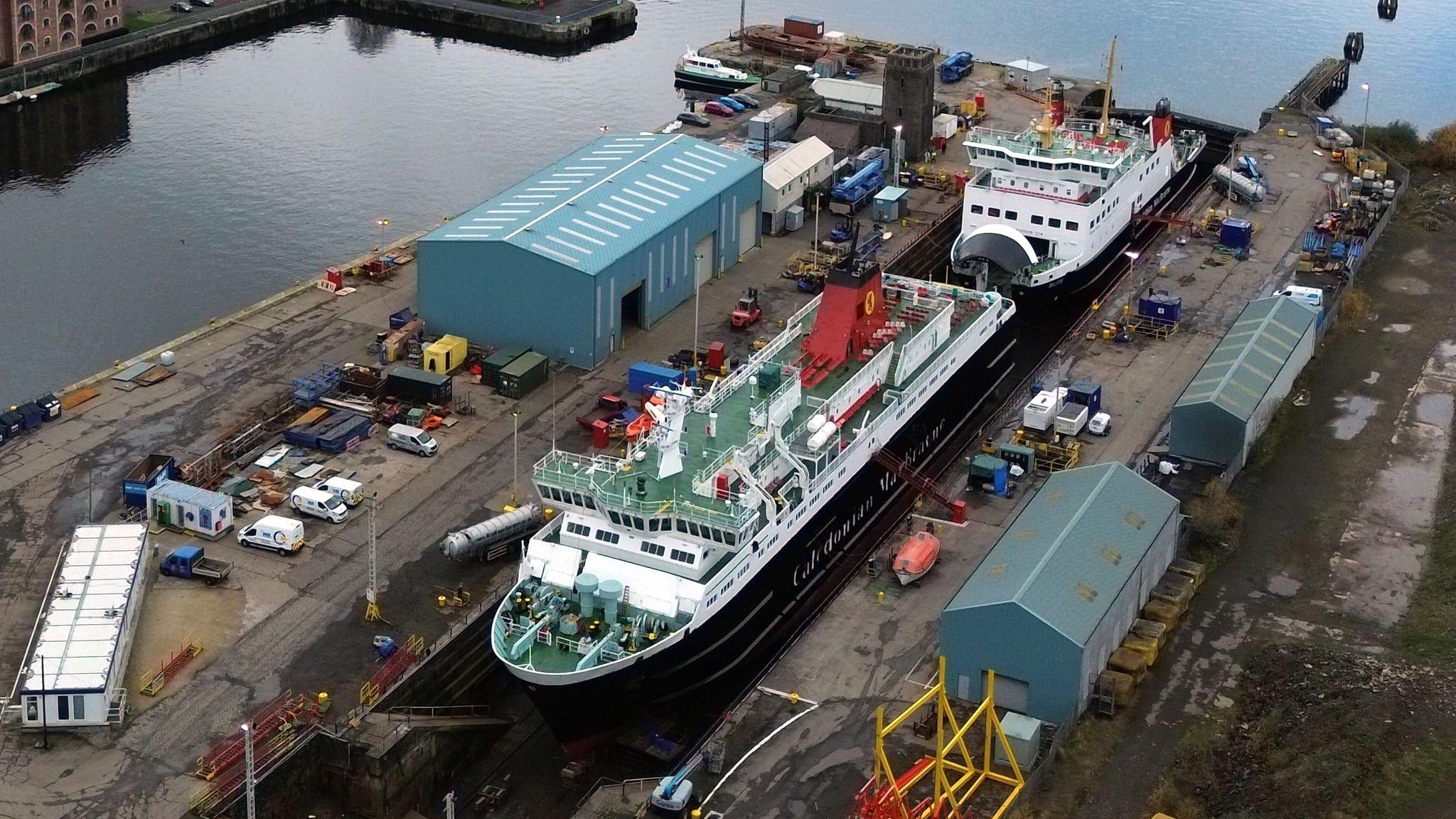 A large black and white ship with red funnels in a dry dock. A smaller vessel is just behind it in the dock