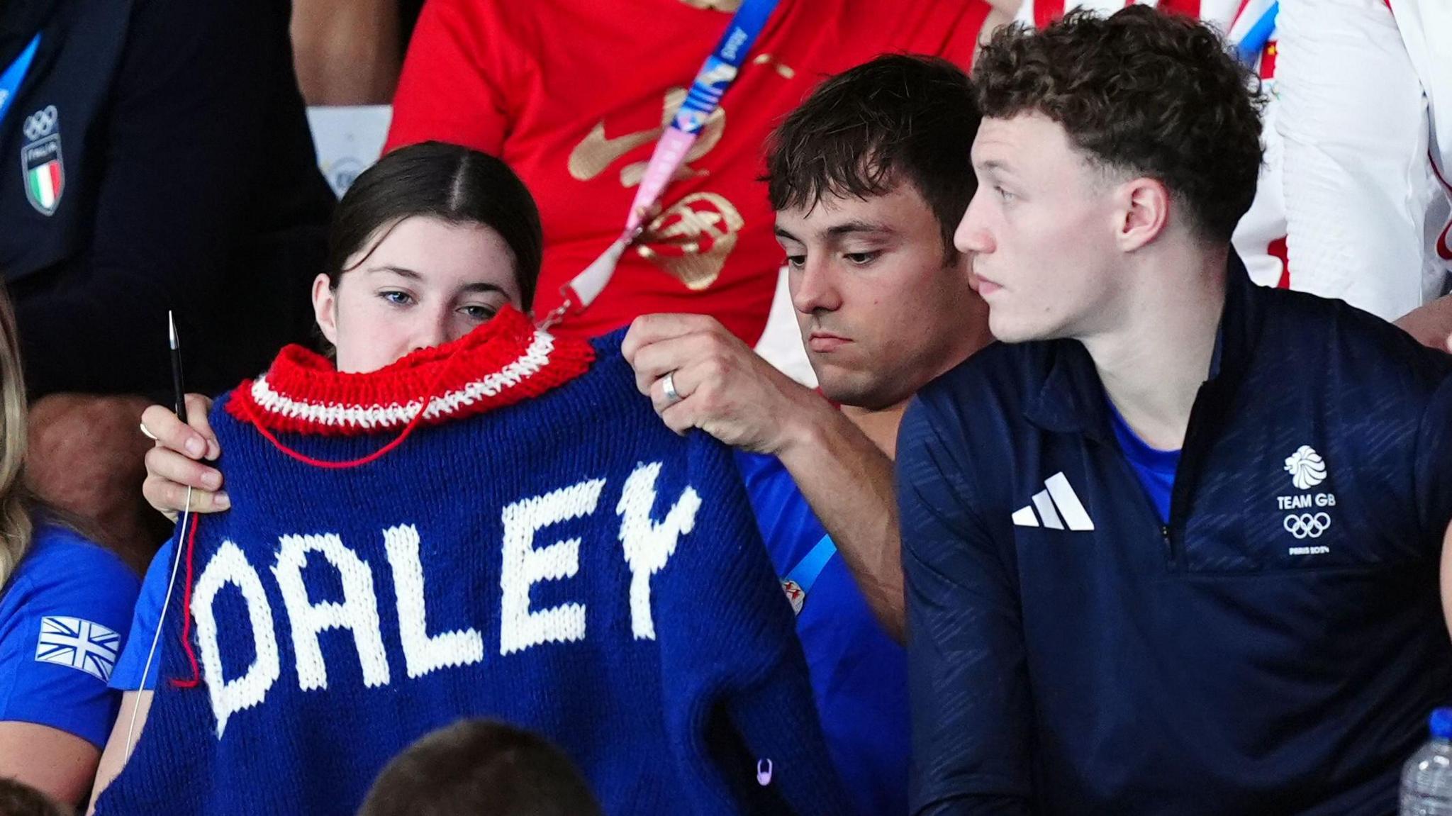 tom daley holding up the jumper he has knitted