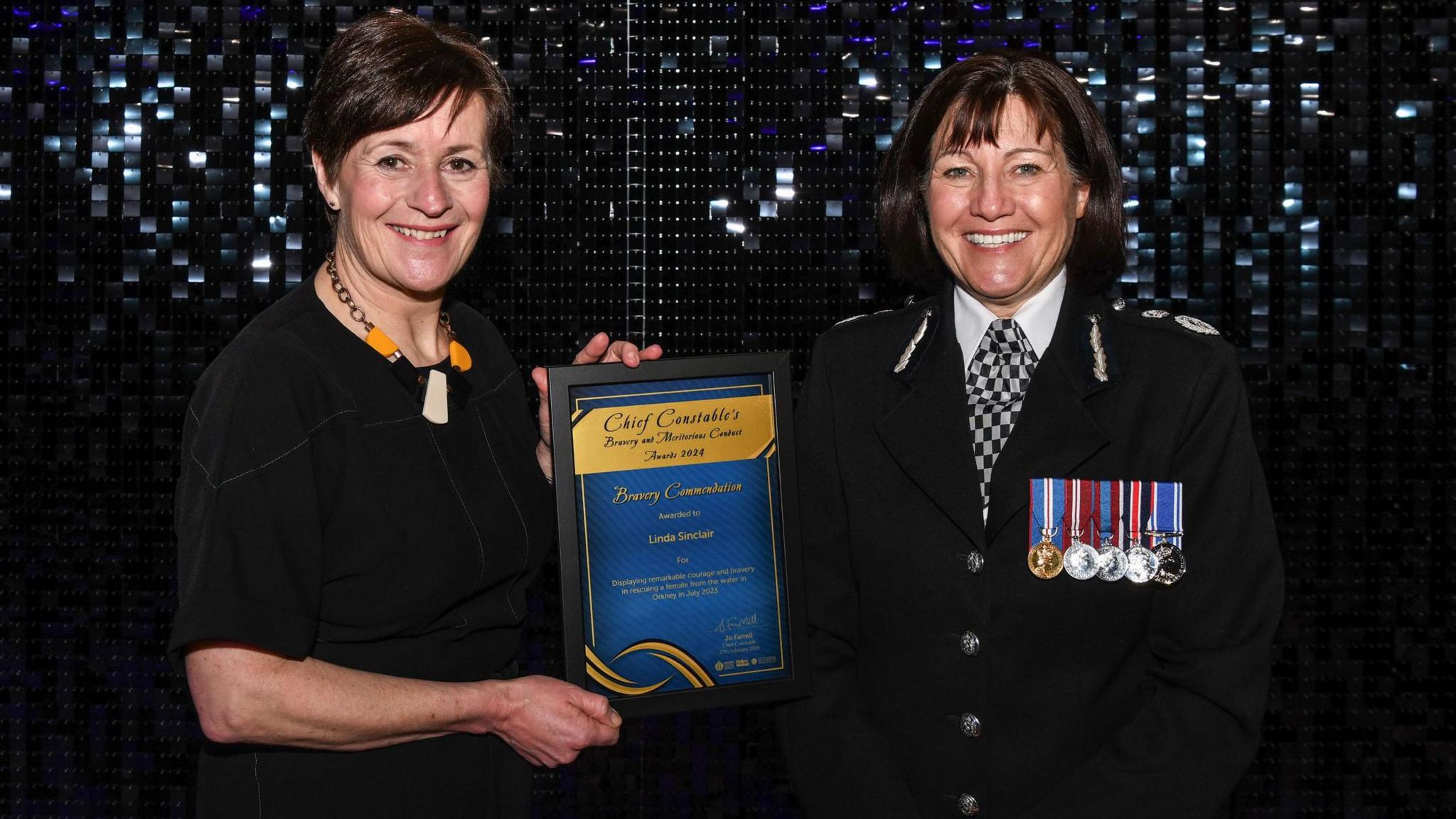 A woman holding a framed bravery certificate standing next to the female chief constable of Police Scotland