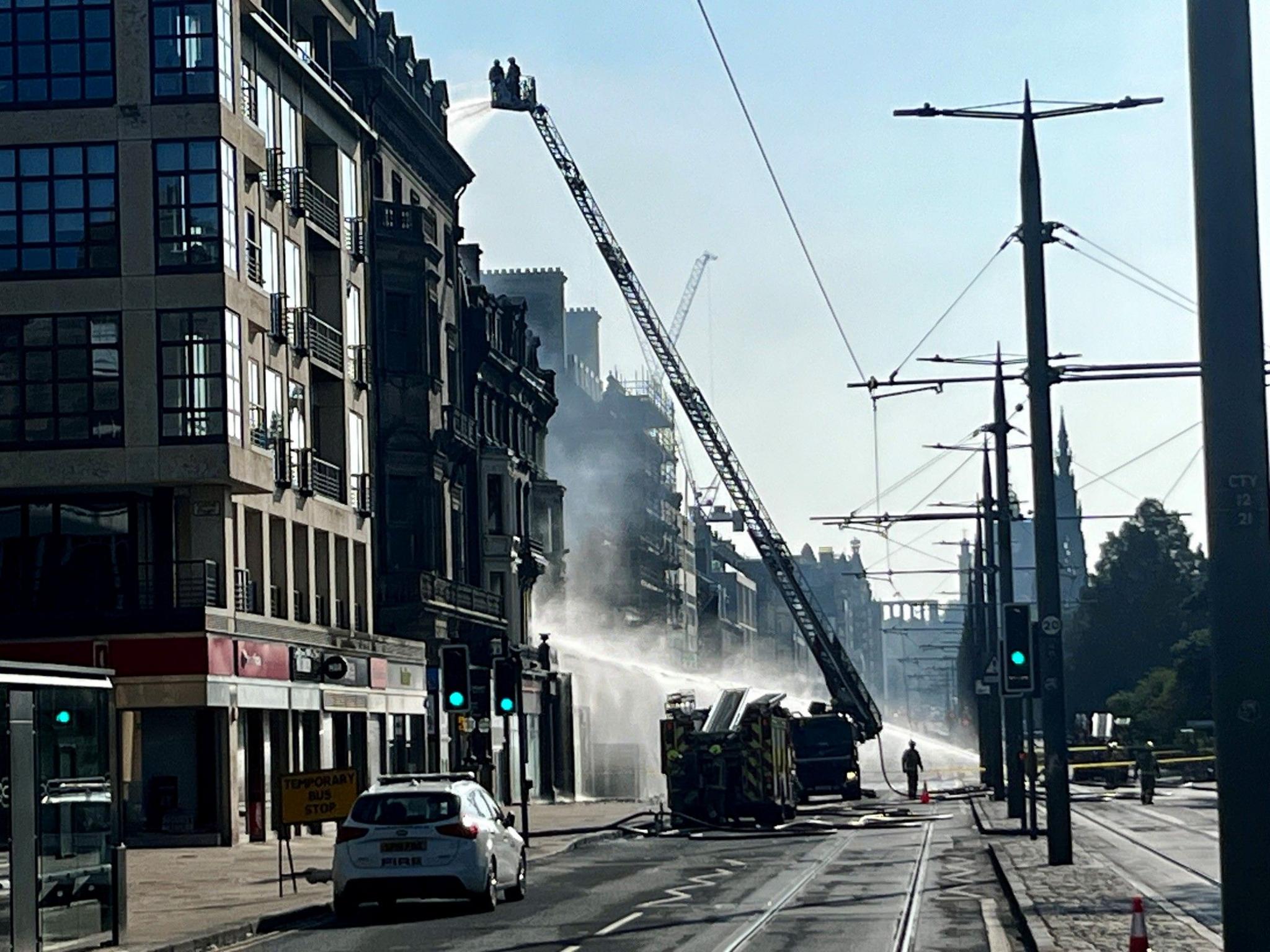 A high reach fire engine reaching up to a a building. A hose is also spraying water across the street.