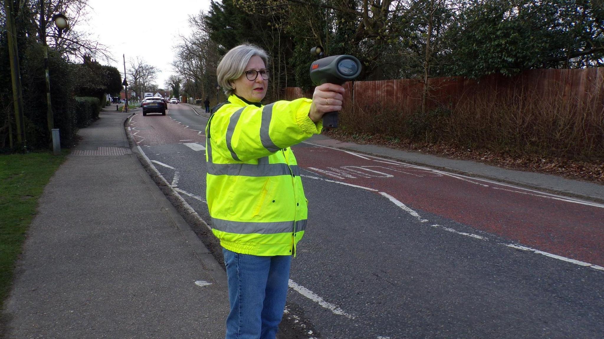 A Speedwatch volunteer holding a speed gun at the roadside