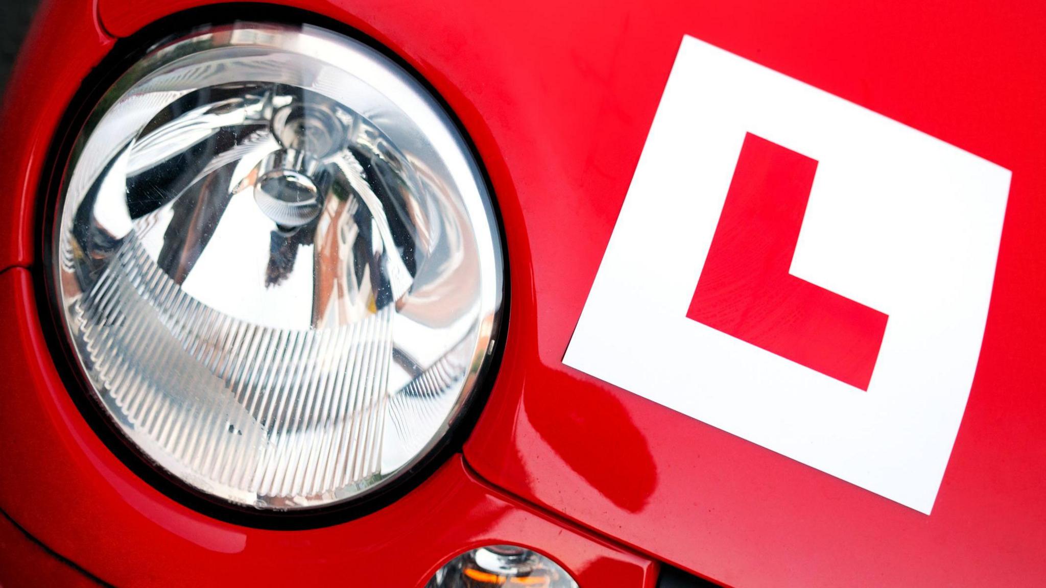 A red car with an L plate sticker on front bonnet to indicate the car is being driven by a learner driver