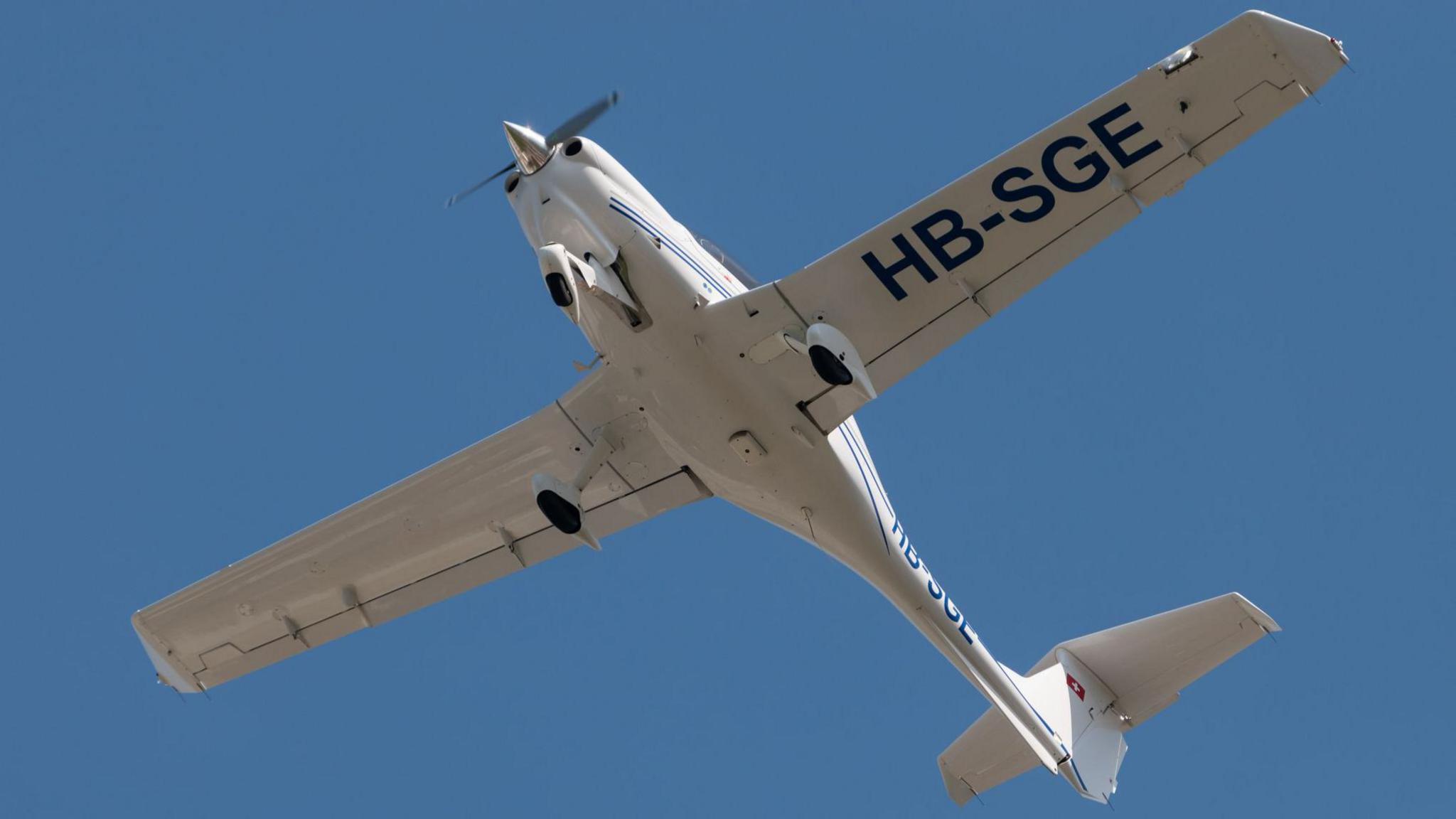 The underside of a white DA40 aircraft against the blue backdrop of the sky