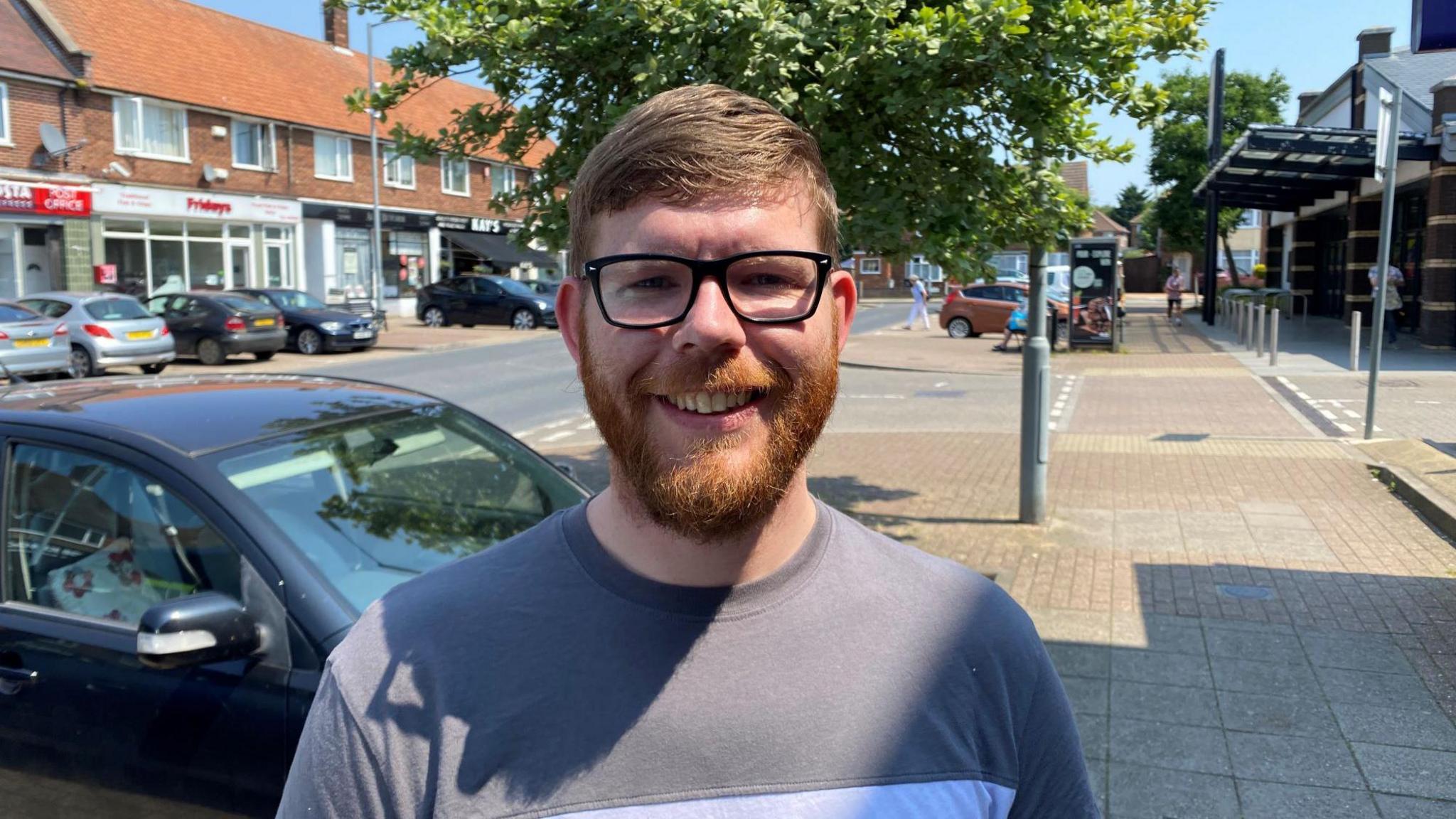 Bearded man in glasses and wearing blue T-shirt smiling to camera