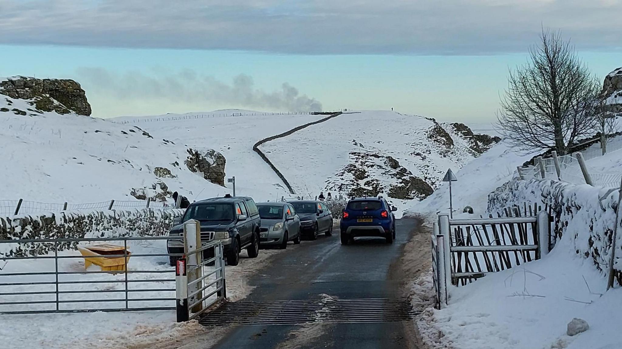 Three parked cars along a snowy stretch of road with one driving past