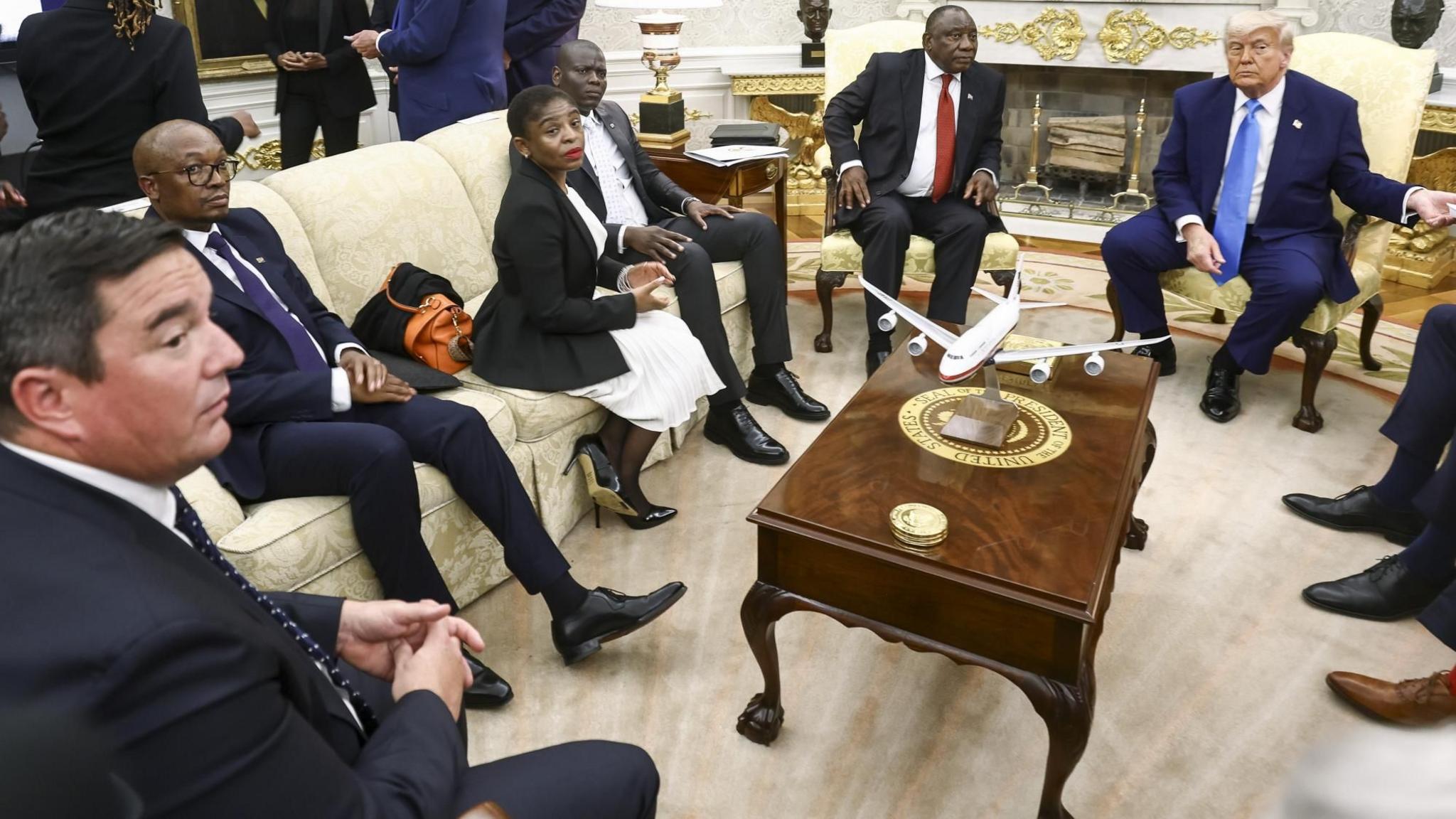 Five members of the South Africa delegation seen sitting in the Oval Office with Donald Trump seated on the right in a dark blue suit and light blue tie. John Steenhuisen, in a dark suit and tie, is sitting to the left of the shot and Cyril Ramaphosa, in a black suit and red tie, is next to Trump - 21 May 2025.