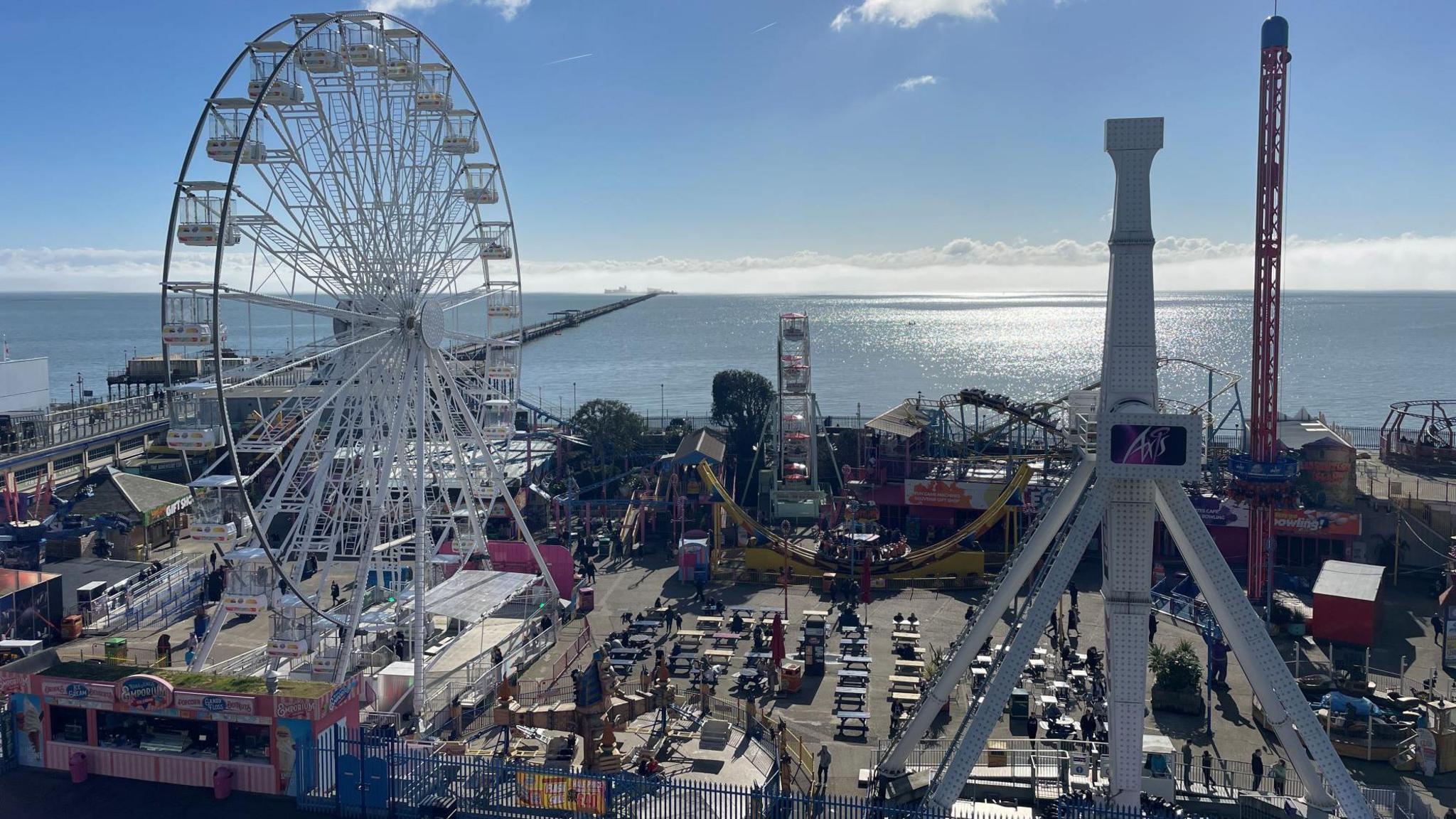 The pleasure beach at Southend. The sea is in the distance with a large ferris wheel and other fairground attractions in the foregrounds.