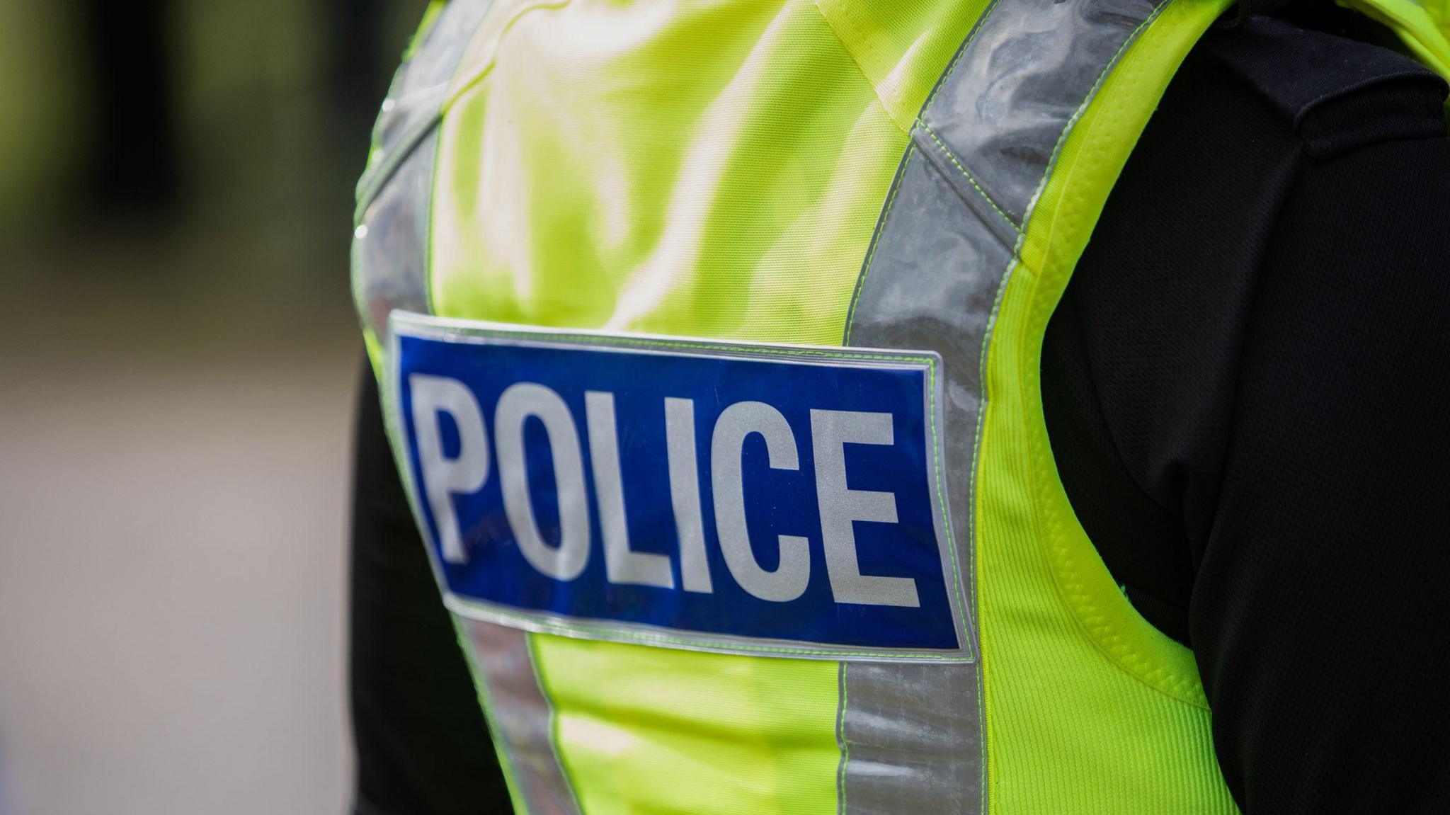 A police officer wearing a black top and a hi-vis vest with a "police" label on the back