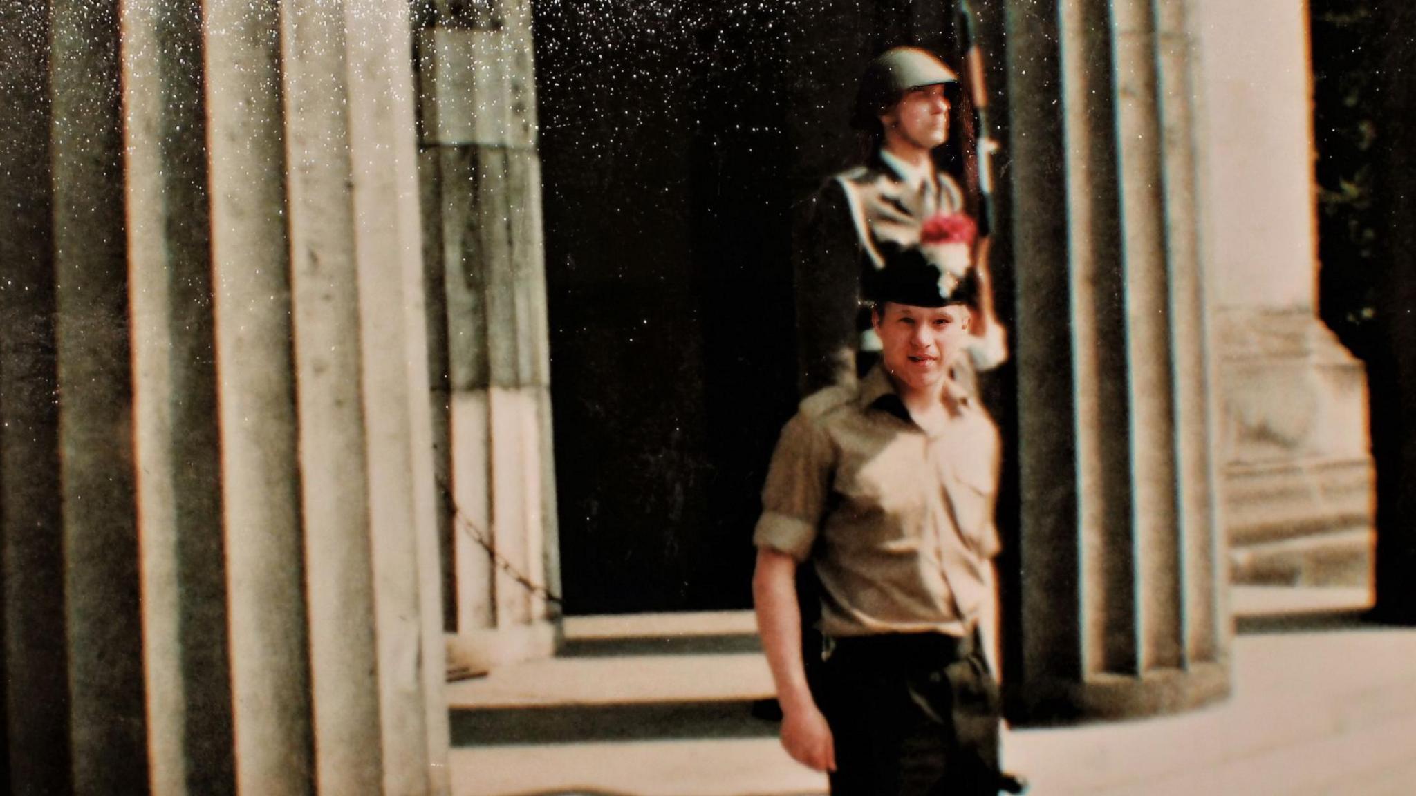 An archive picture of a soldier posing at the camera. In the background you can see a guardsman holding a rifle looking away from the camera