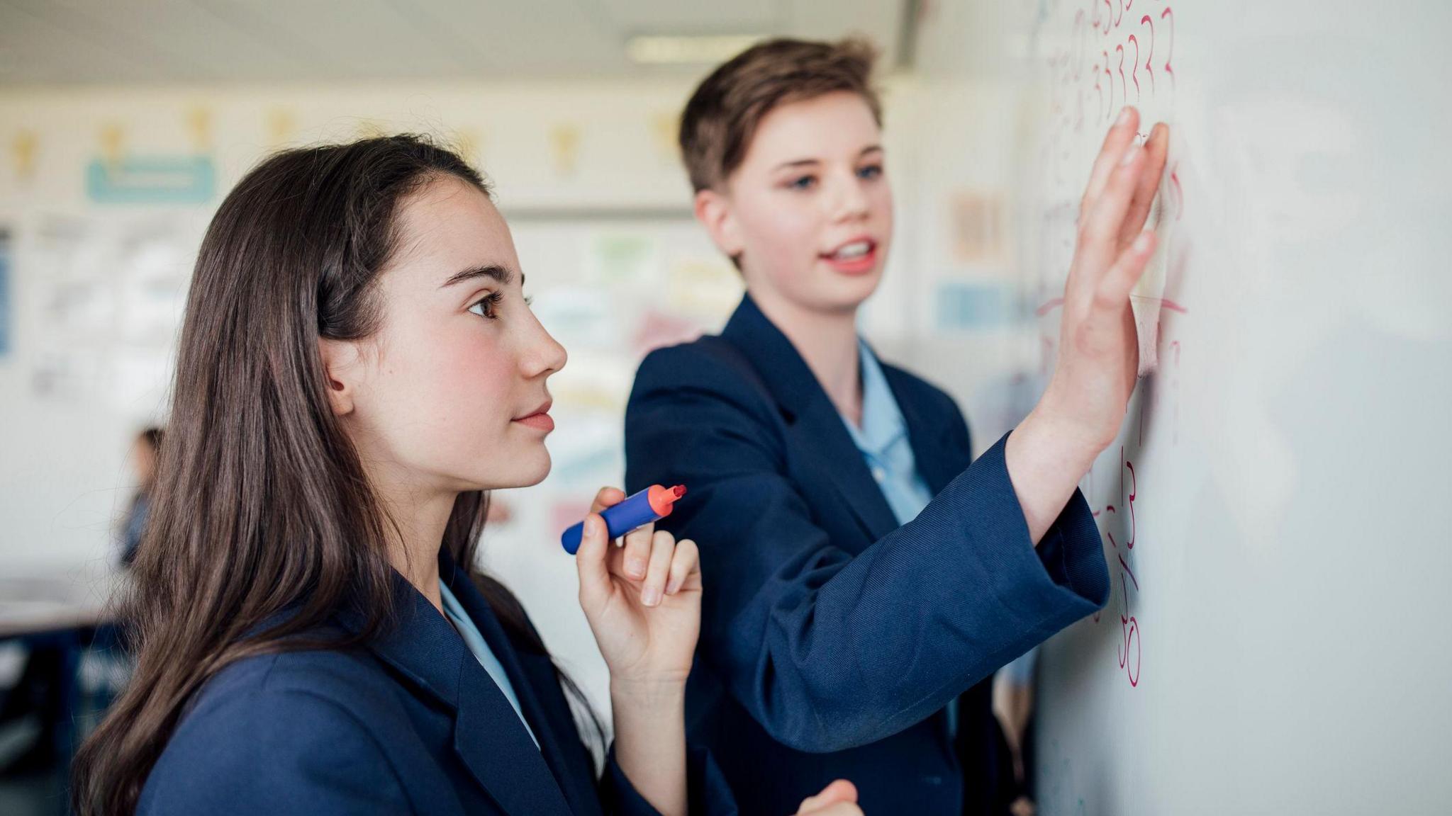 Stock image of a teenage girl and boy at a whiteboard, doing a maths problem together