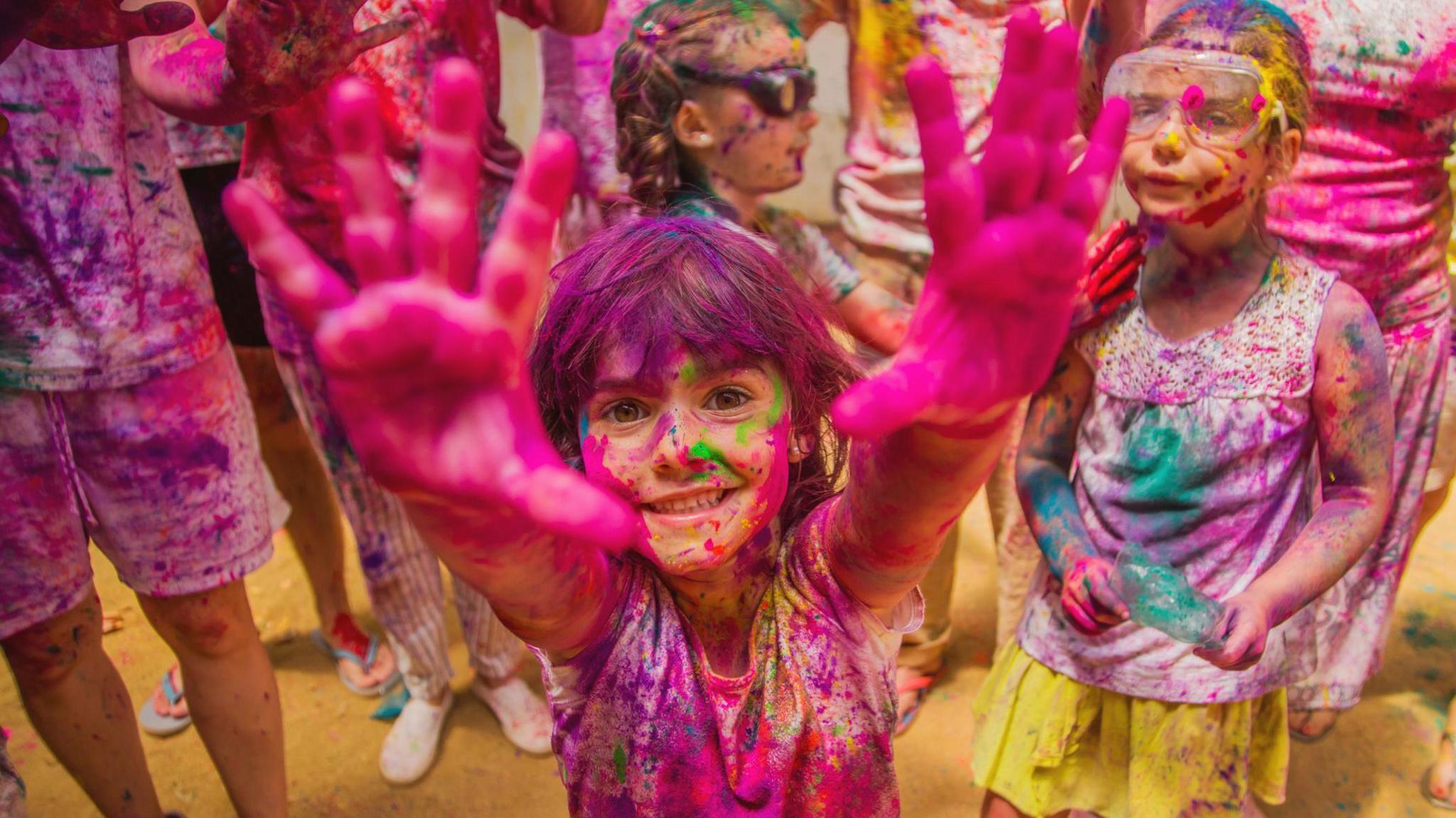 A child is covered in colourful paint powder, holding their hands up to the camera