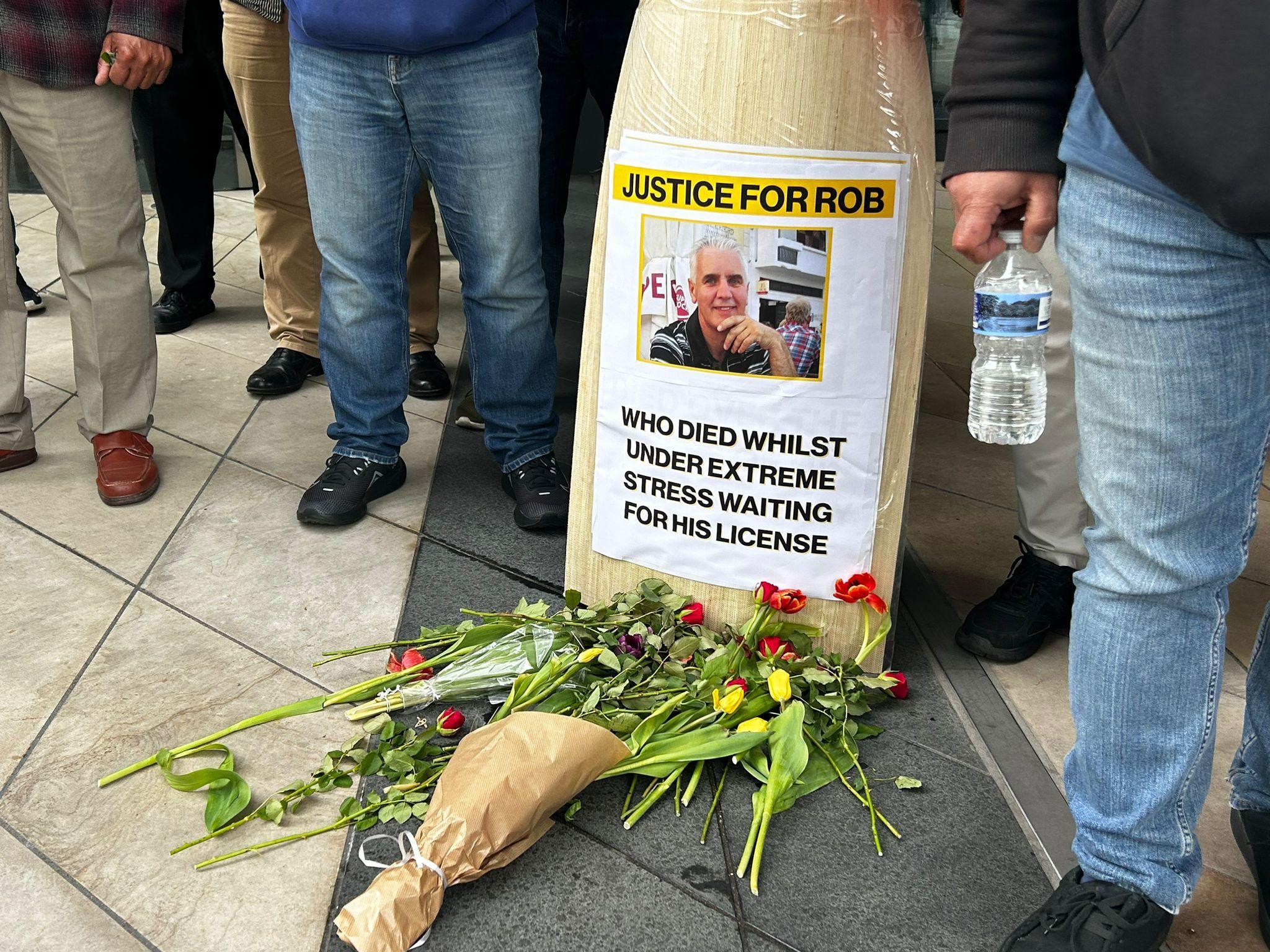 A poster reading 'justice for rob who died whilst under extreme stress waiting for his licence'