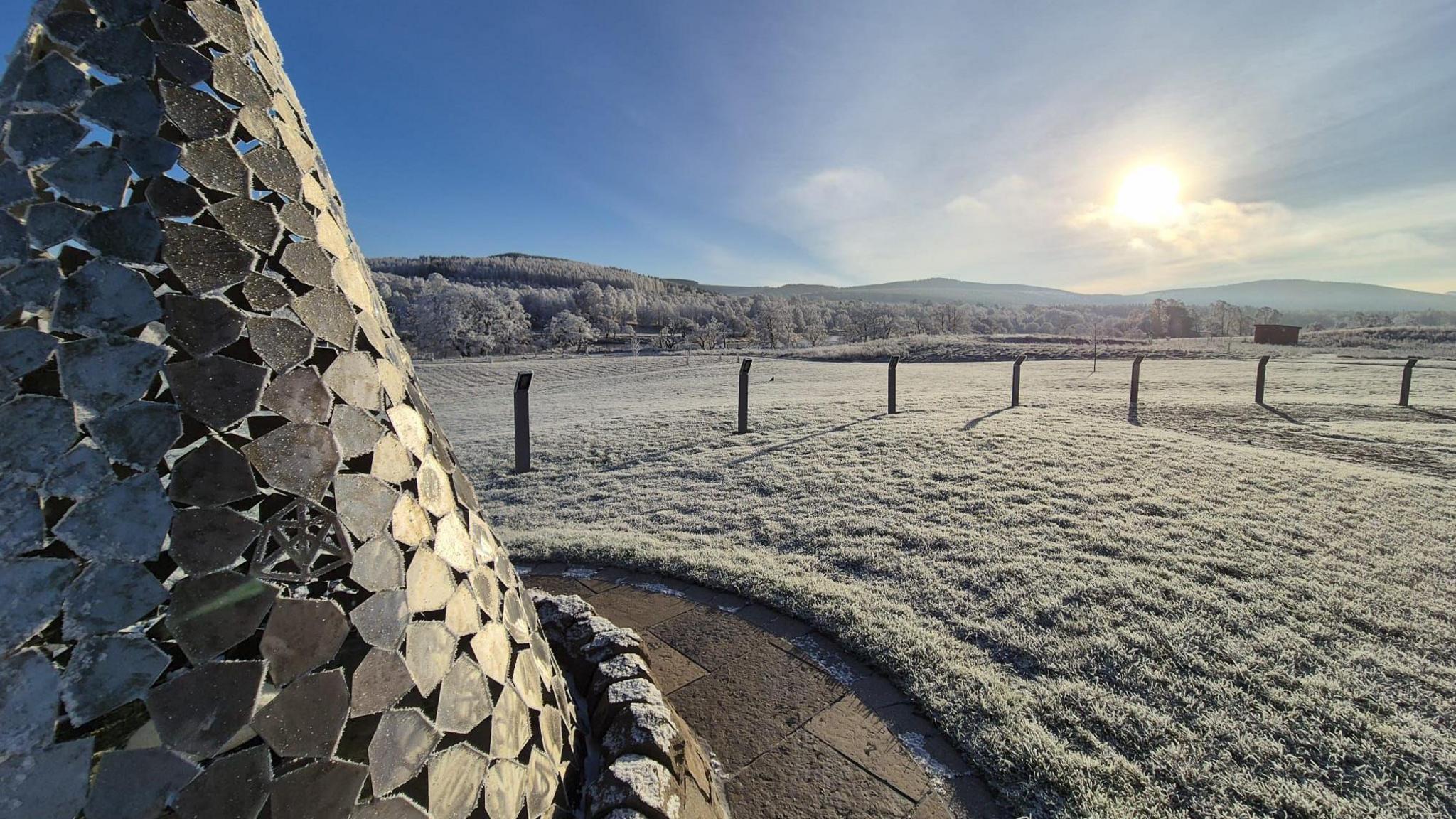 Frost covers the ground in the morning near the Cairngorm mountains. A sculpture also glistens, covered in ice. In the distance, the mountains Carn na loinne and carn na coinnse xan be seen.