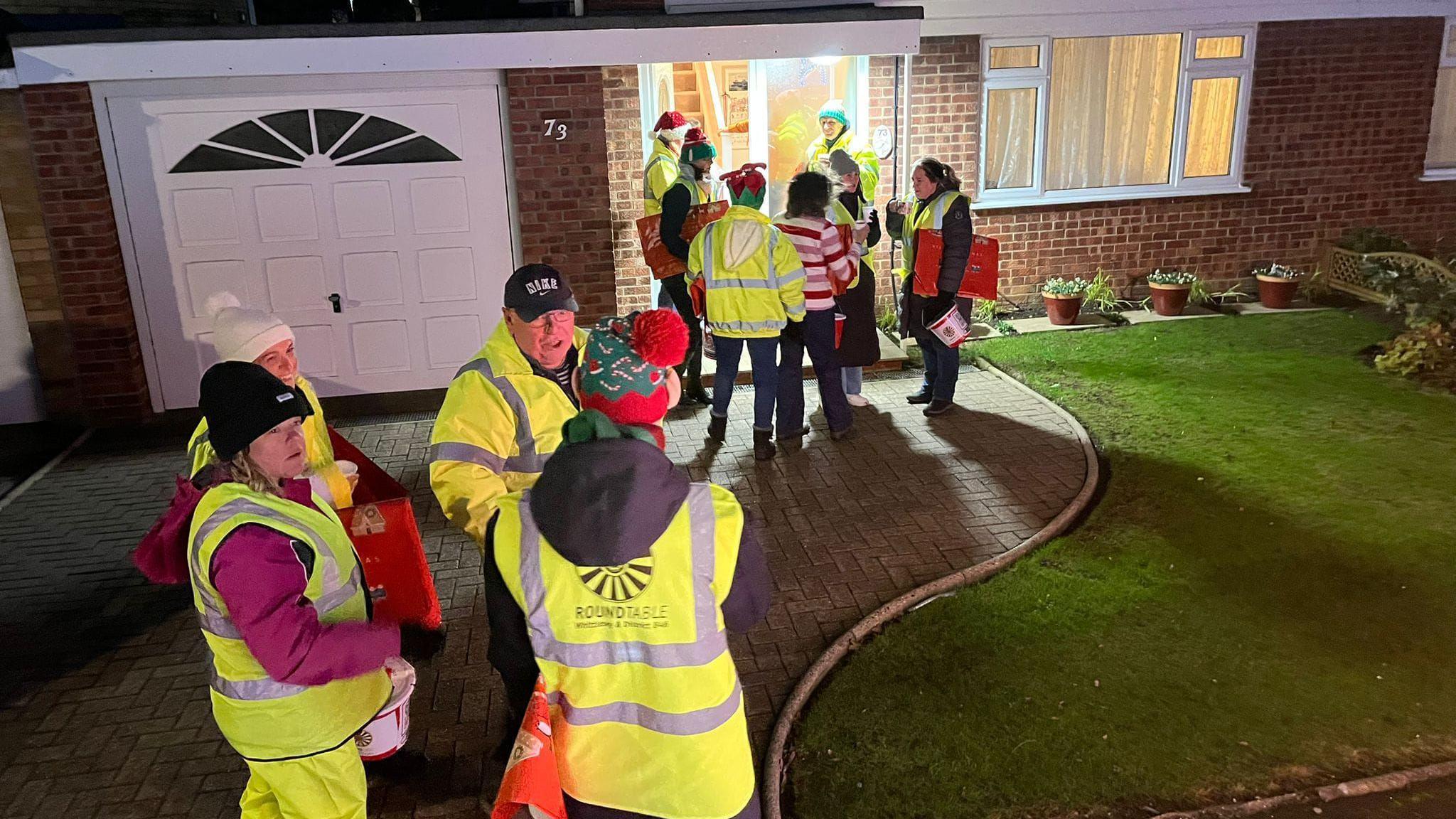 Volunteers wearing a high-visibility green jacket standing on a drive way 