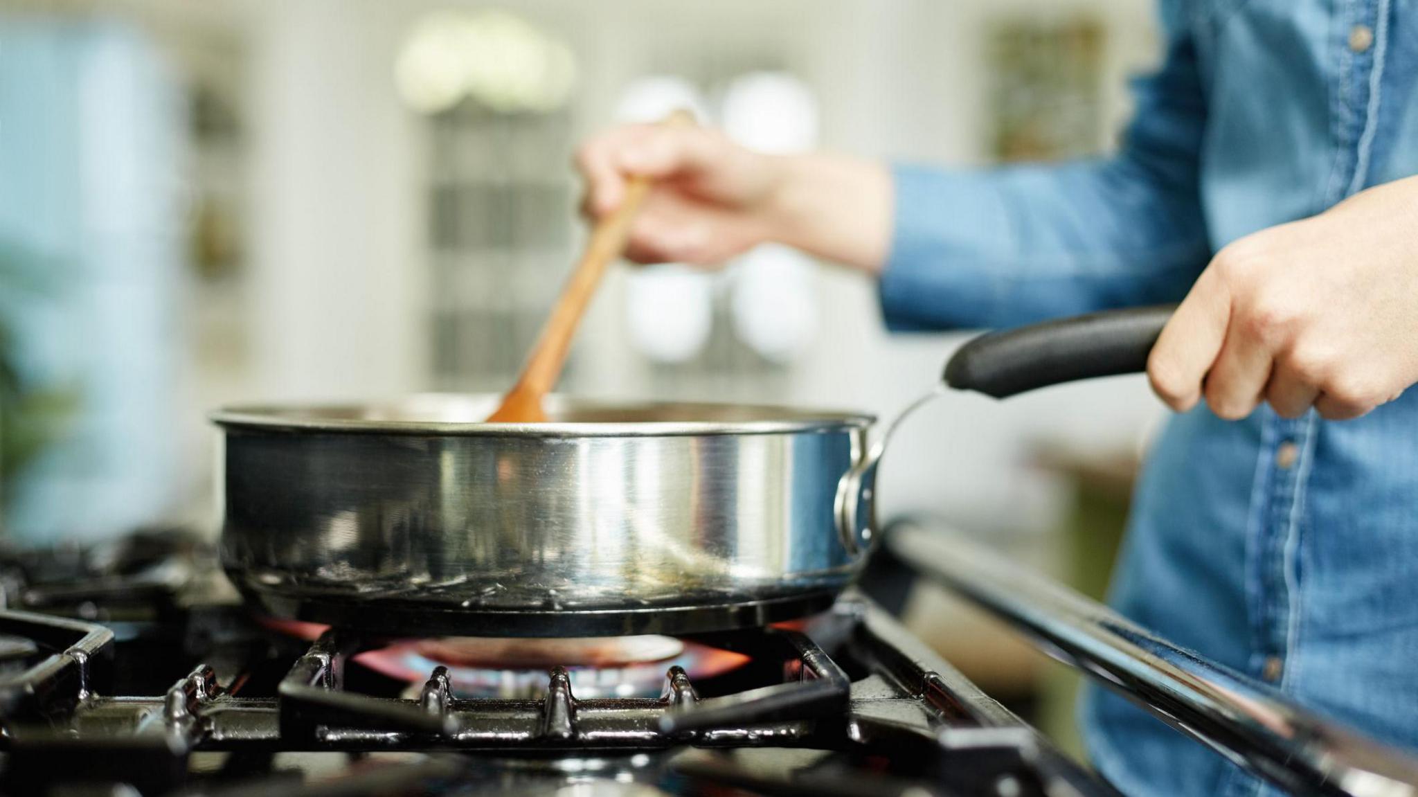 Close-up midsection image of woman cooking food in frying pan. Utensil is placed on gas stove.