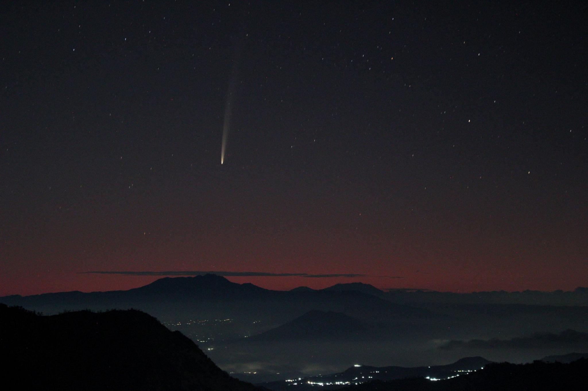 A mountainous region against a night sky backdrop, with a clear, long bright streak of light heading from top to bottom. 