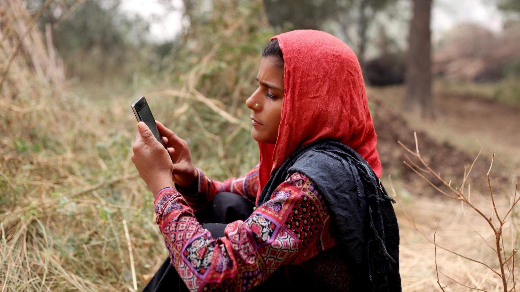 An Indian woman using a mobile phone outdoors in a rural setting