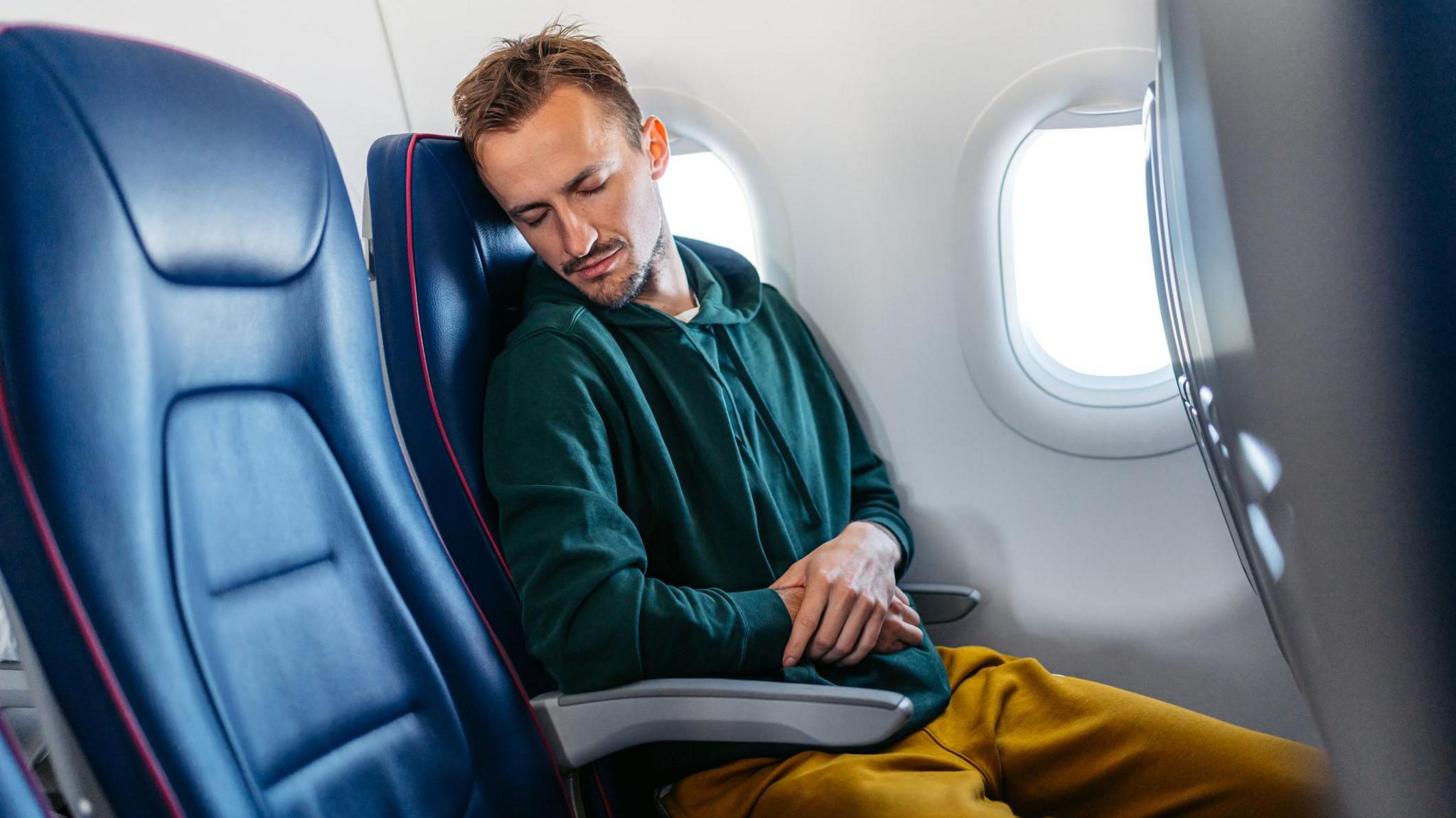 Man asleep on plane with both arms on armrests