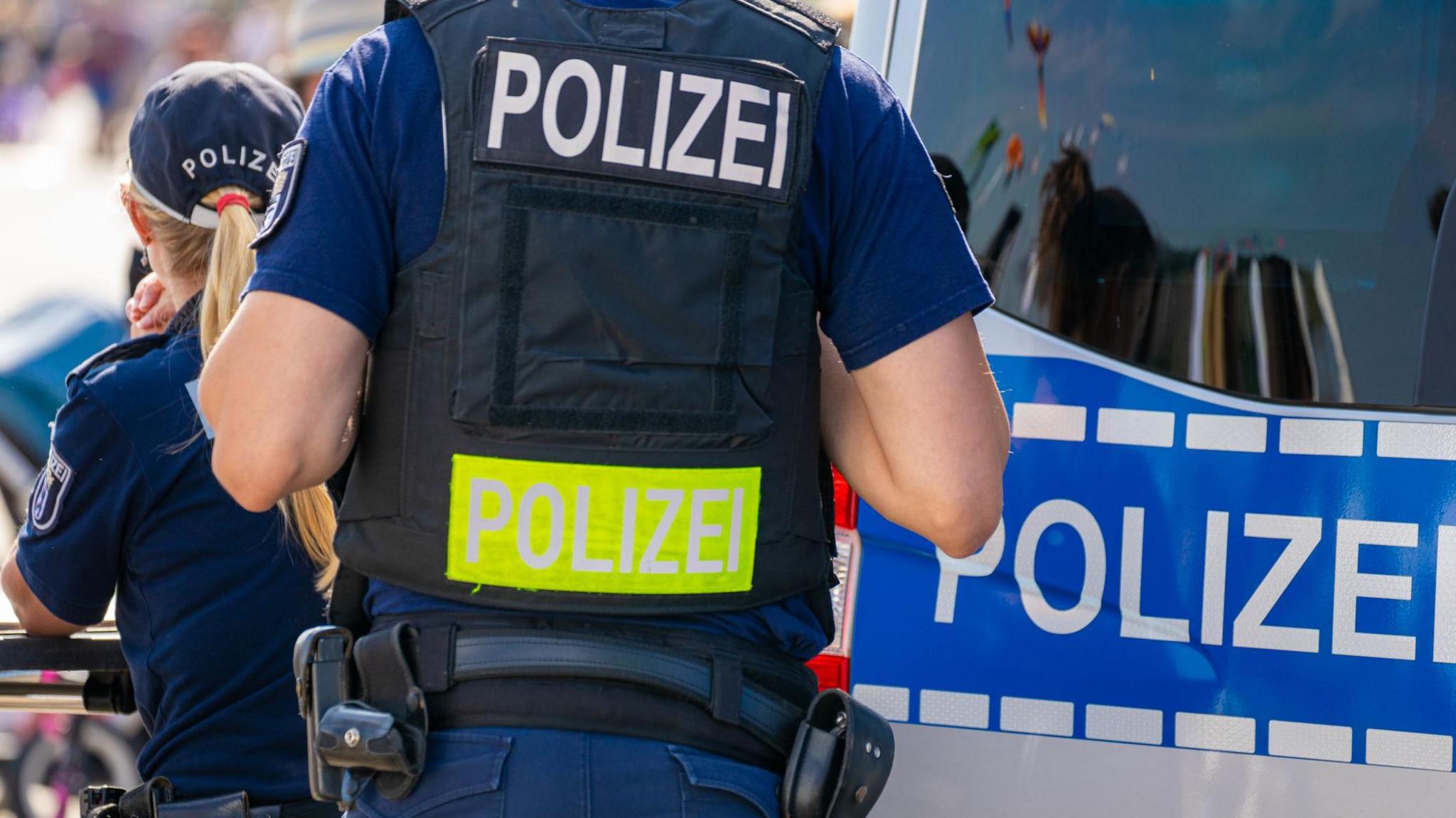 A policeman stands facing a Polizei vehicle. 