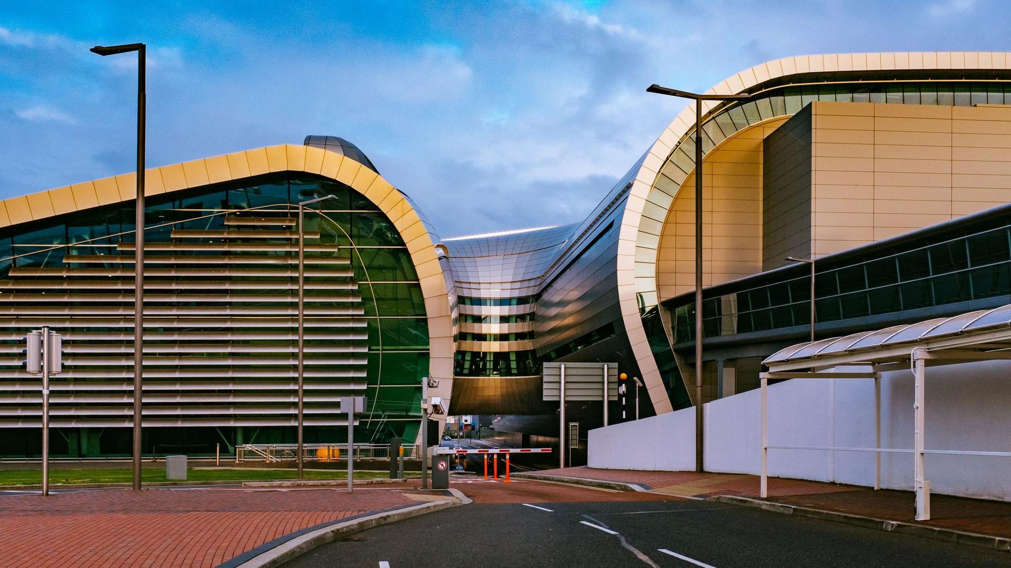 The outside of Dublin Airport. It is a large curved building with steel panels and glass sides.