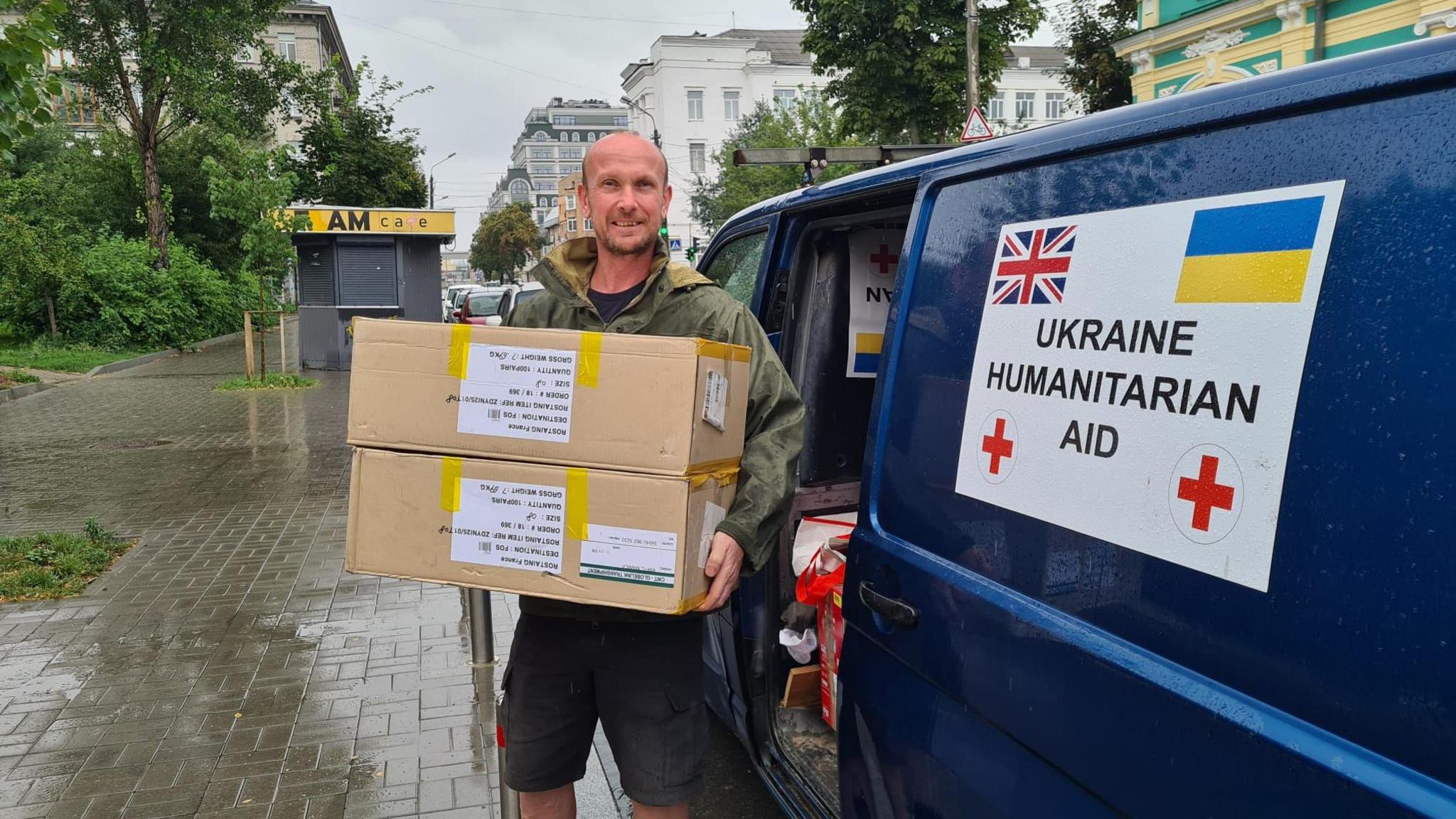 Brian Hammond carrying boxes of supplies. He is standing next to a van with a "Ukraine Humanitarian Aid" sign on the side