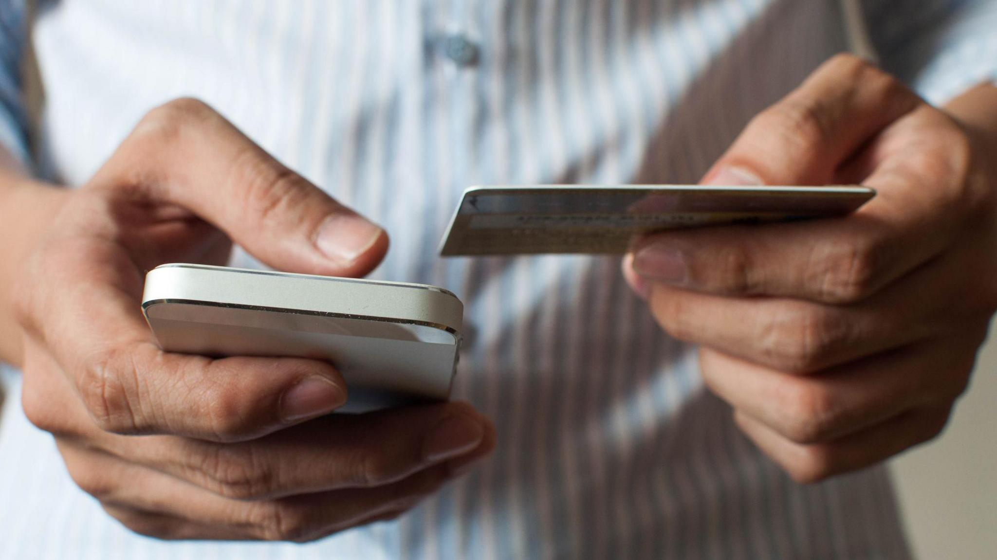 A person holds a phone in one hand and a bank card in the other.