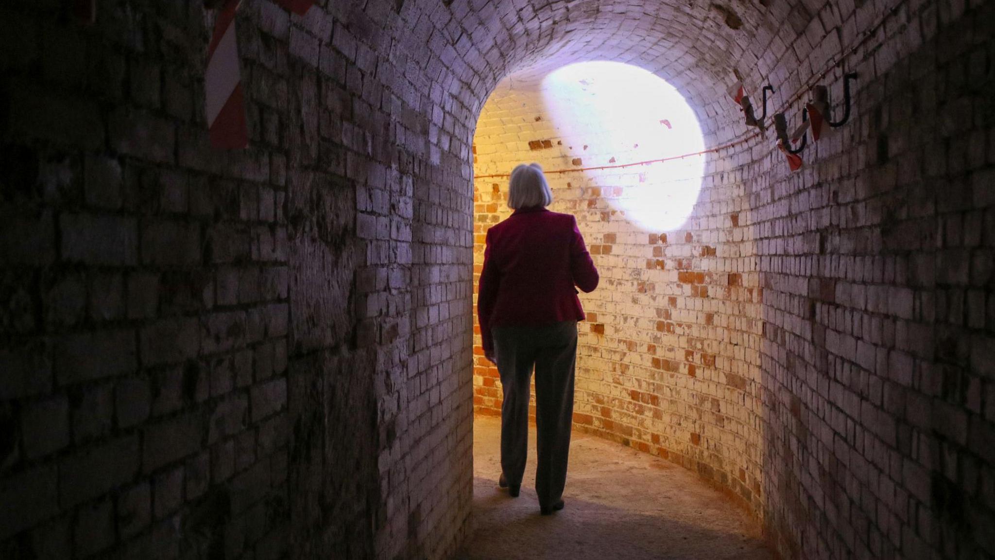 woman in a darkened underground passage shining her torch at brickwork