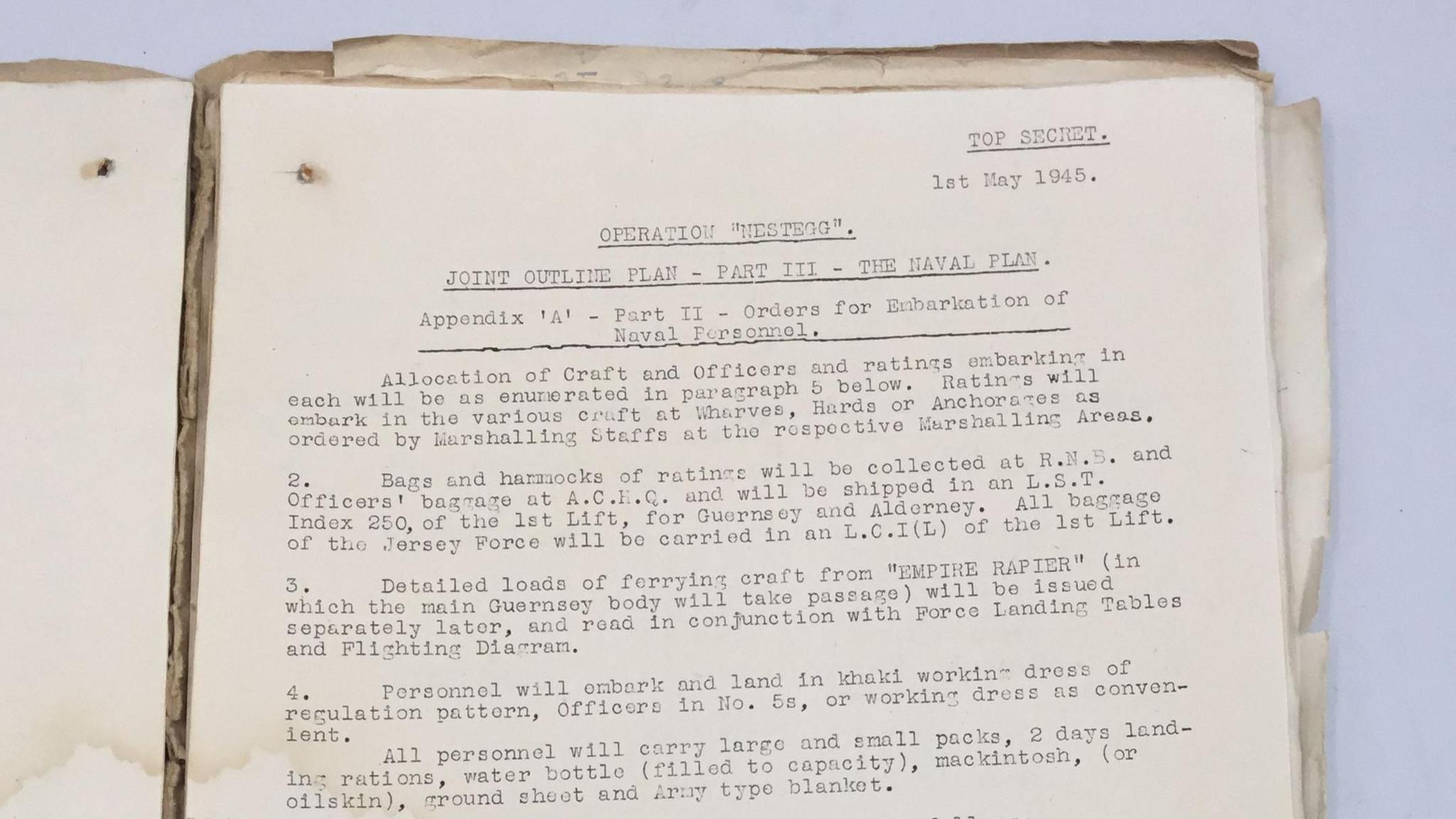 An old document in a manila folder. It reads: TOP SECRET. Ist May 1945. OPERATION "NESTEGG". JOINT OUTLINE PLAN - PART ITI - THE NAVAL PLAN Appendix 'A' - Part II - Orders for Enbarkation of - Naval Personnel. Allocation of Craft and Officers and ratings embarking in each will be as enumerated in paragraph 5 below. Ratings will embark in the various craft at Wharves, Hards or Anchorages as ordered by Marshalling Staffs at the rospoctive Marshalling Areas. Bags and harmocks of ratings will be collected at R.N.5. and Officers' bagrage at A.C.F.C. and will be shipped in an L.S.T. Index 250, of the lst Lift, for Guernsey and Alderney. All bagrage of the Jersey Force will be carried in an L.C.I (L) of the lst Lift. Detailed loads of forrying craft from "EMPIRE RAPIER" (in which the main Guernsey body will take passage) will be issued separately later, and read in conjunction with Force Landing Tables and Flighting Diarram. 4. Personnel will embark and land in khaki working dress of regulation pattern, Officers in No. 5s, or working dress as convenient. All personnel will carry largo and small packs, 2 days landing rations, water bottle (filled to capacity), mackintosh, (or oilskin), ground sheet and Army type blanket.