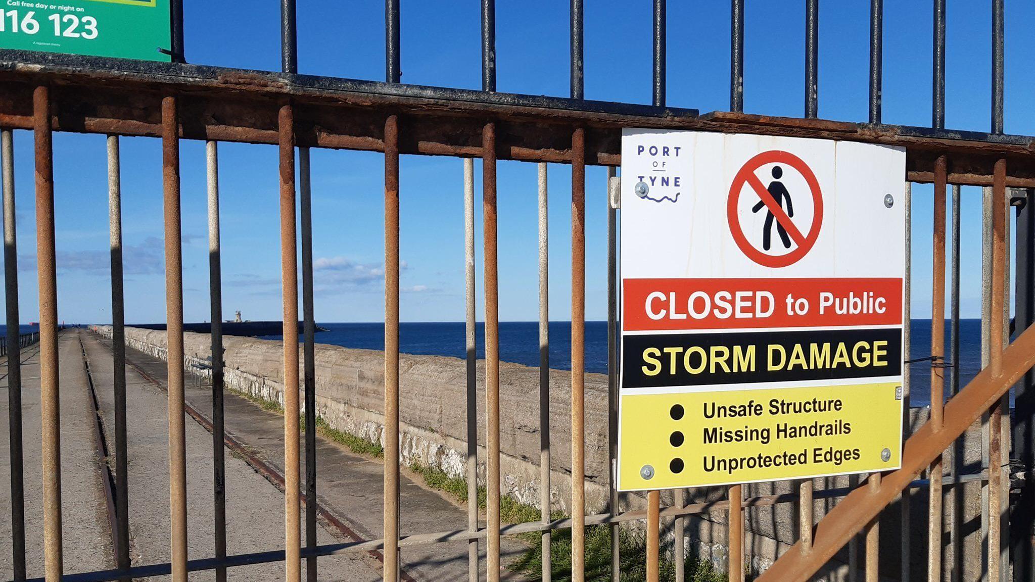 Security fence and warning sign at South Shields pier. The sign reads Closed to Public, Storm Damage. Unsafe Structure. Missing Handrails. Unprotected Edges.   