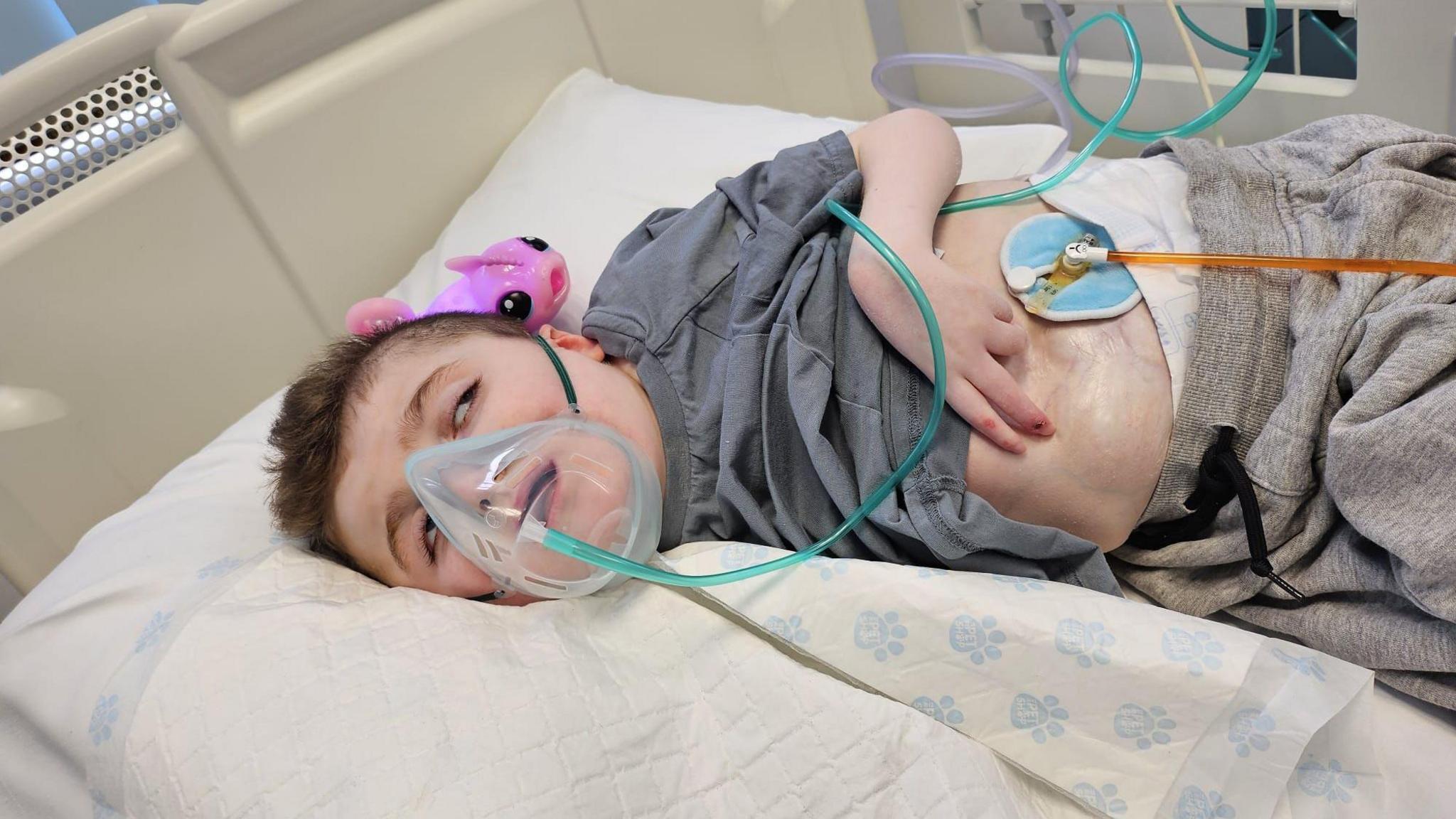 A young boy in a hospital bed wearing an oxygen mask