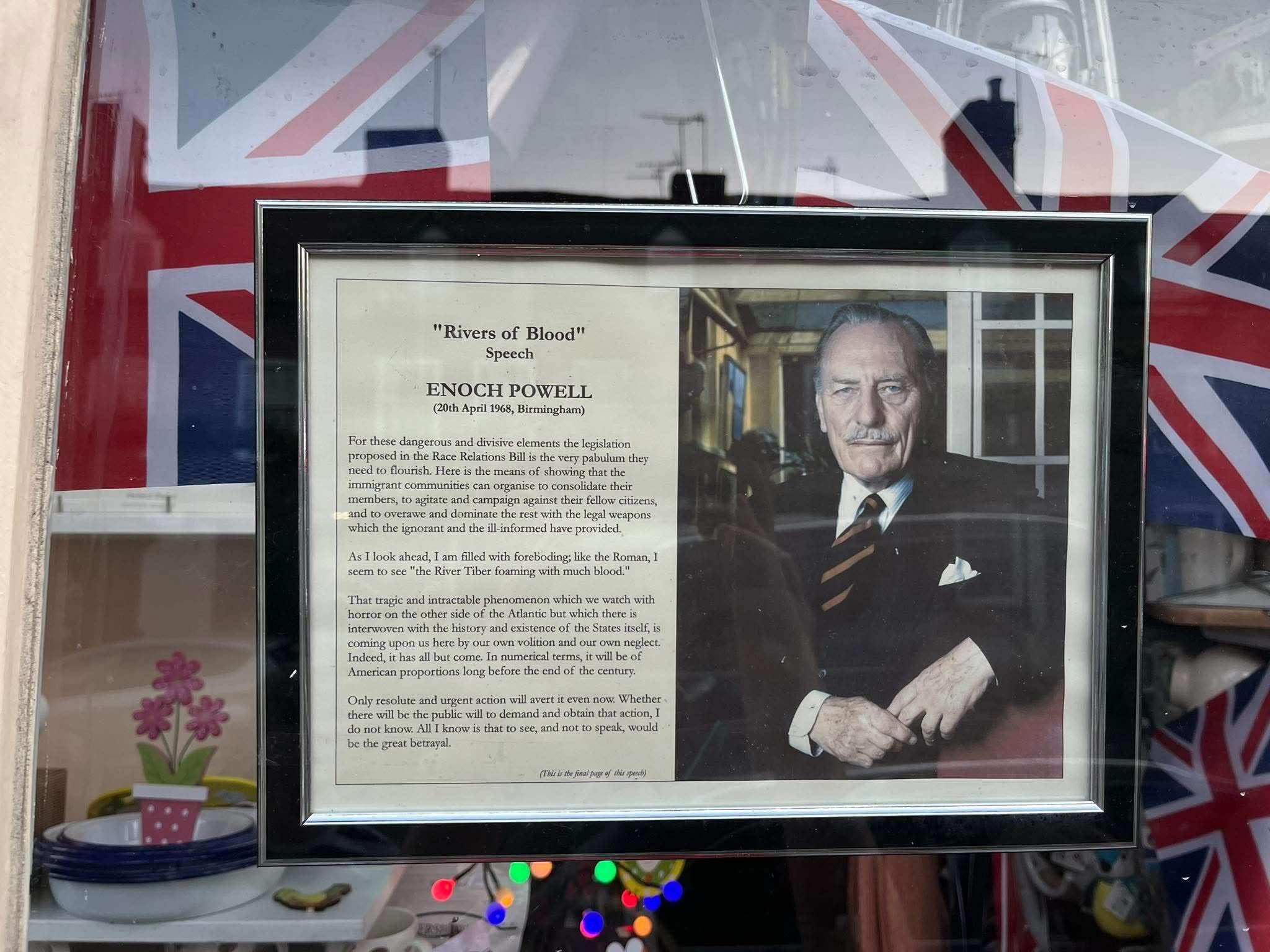 A framed image of a man in a suit and tie next to a text of Enoch Powell's "Rivers of Blood" speech. There are Union flags in the background.