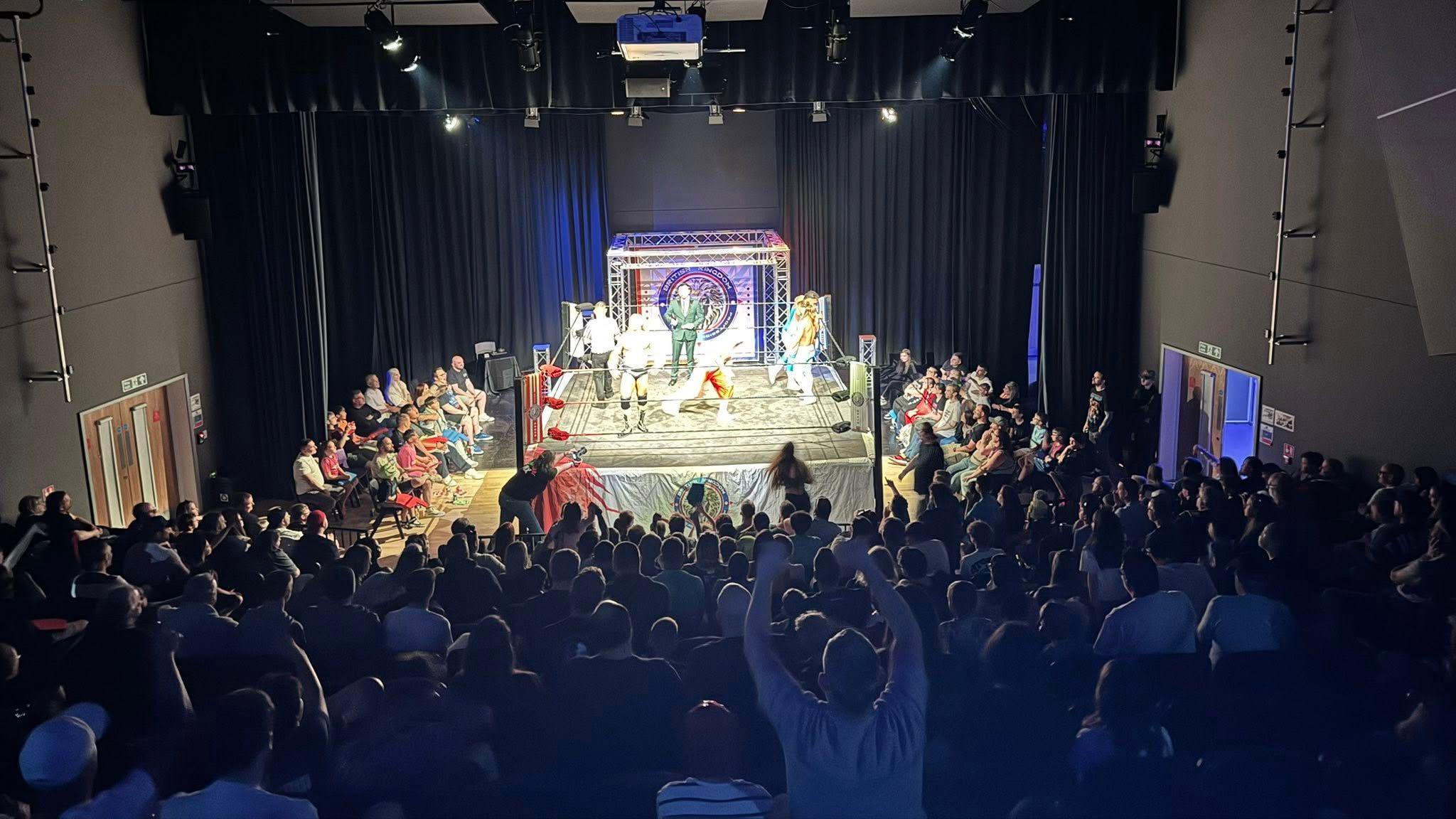 Wrestling fans cheer on the competitors in the ring at the Deanery Theatre in Swindon