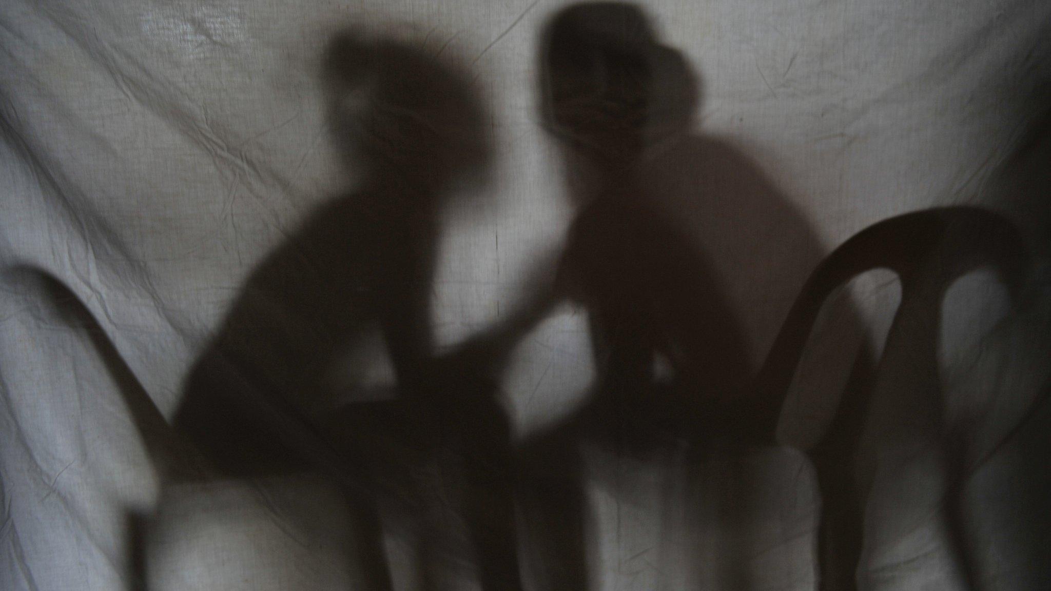 Silhouette of two girls rescued from a sex trafficking ring talking behind a screen